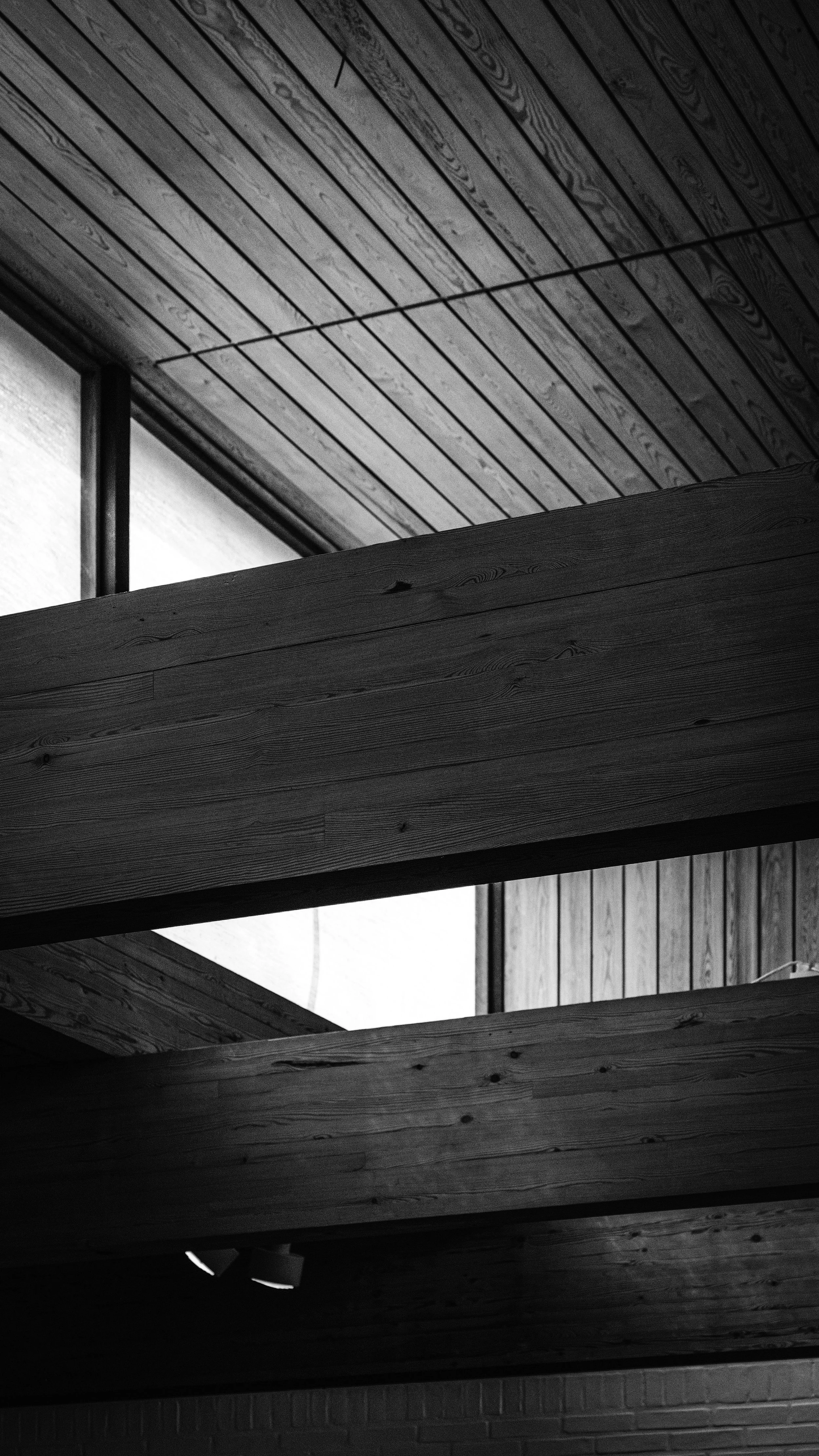Interior ceiling with wooden planks and beams, partially illuminated with natural and artificial light.
