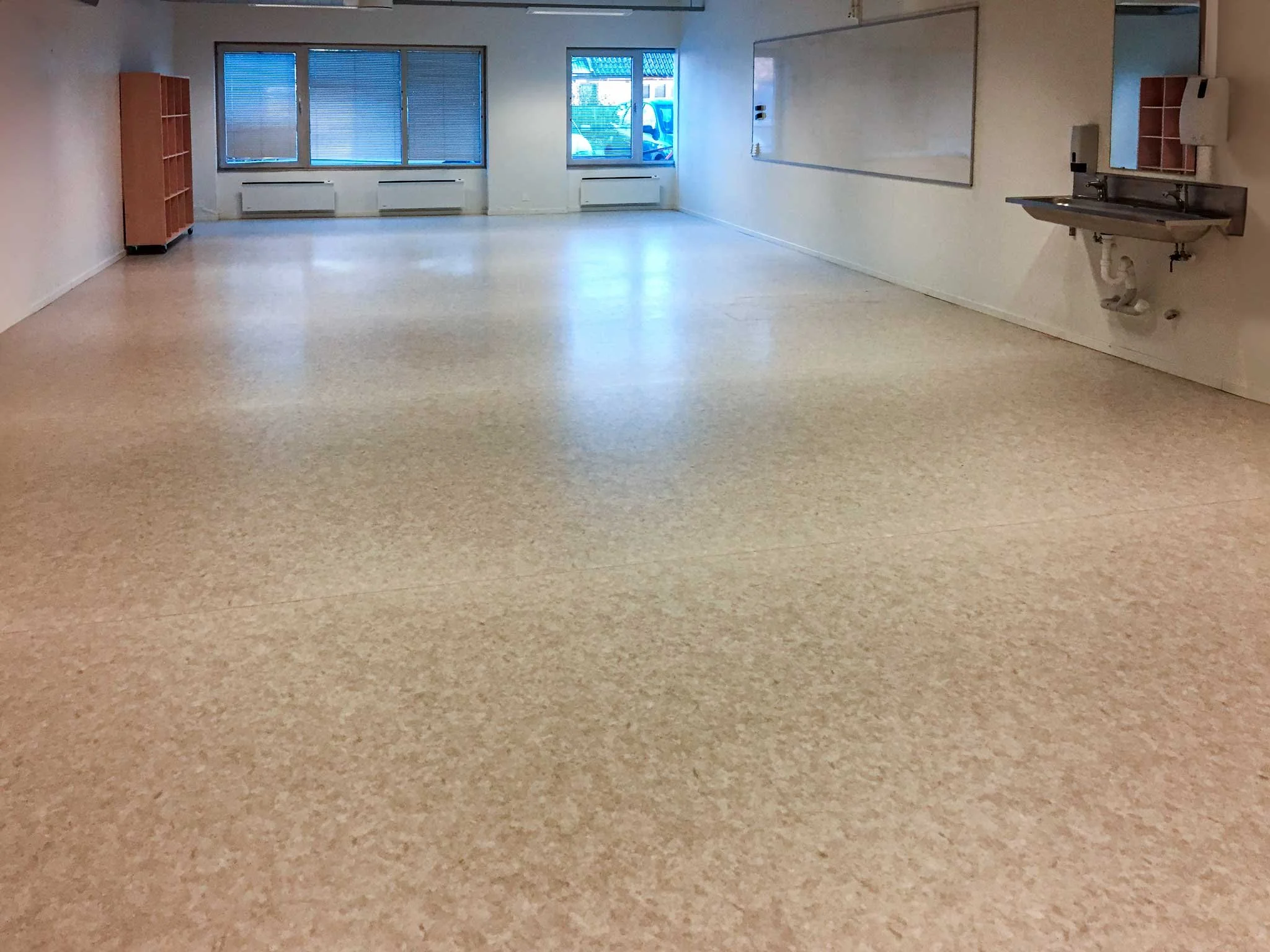 Et tomt kontorlokale på Sortland, med store vinduer, et hvitt tavle, en vask, og hyller på veggen.. Kvartal 20 AS.