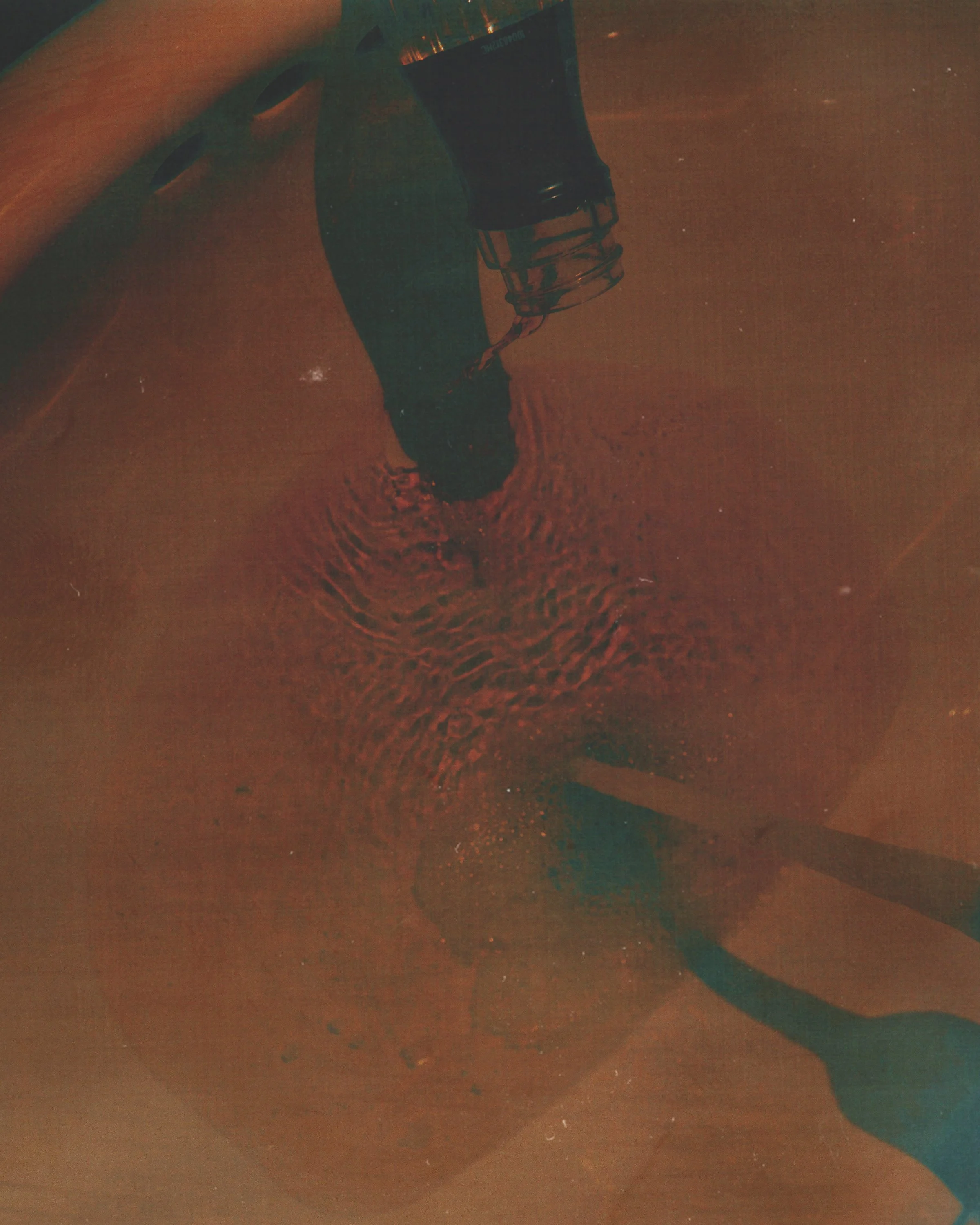 A person drinking from a glass of dark soda; water on the surface with ripples