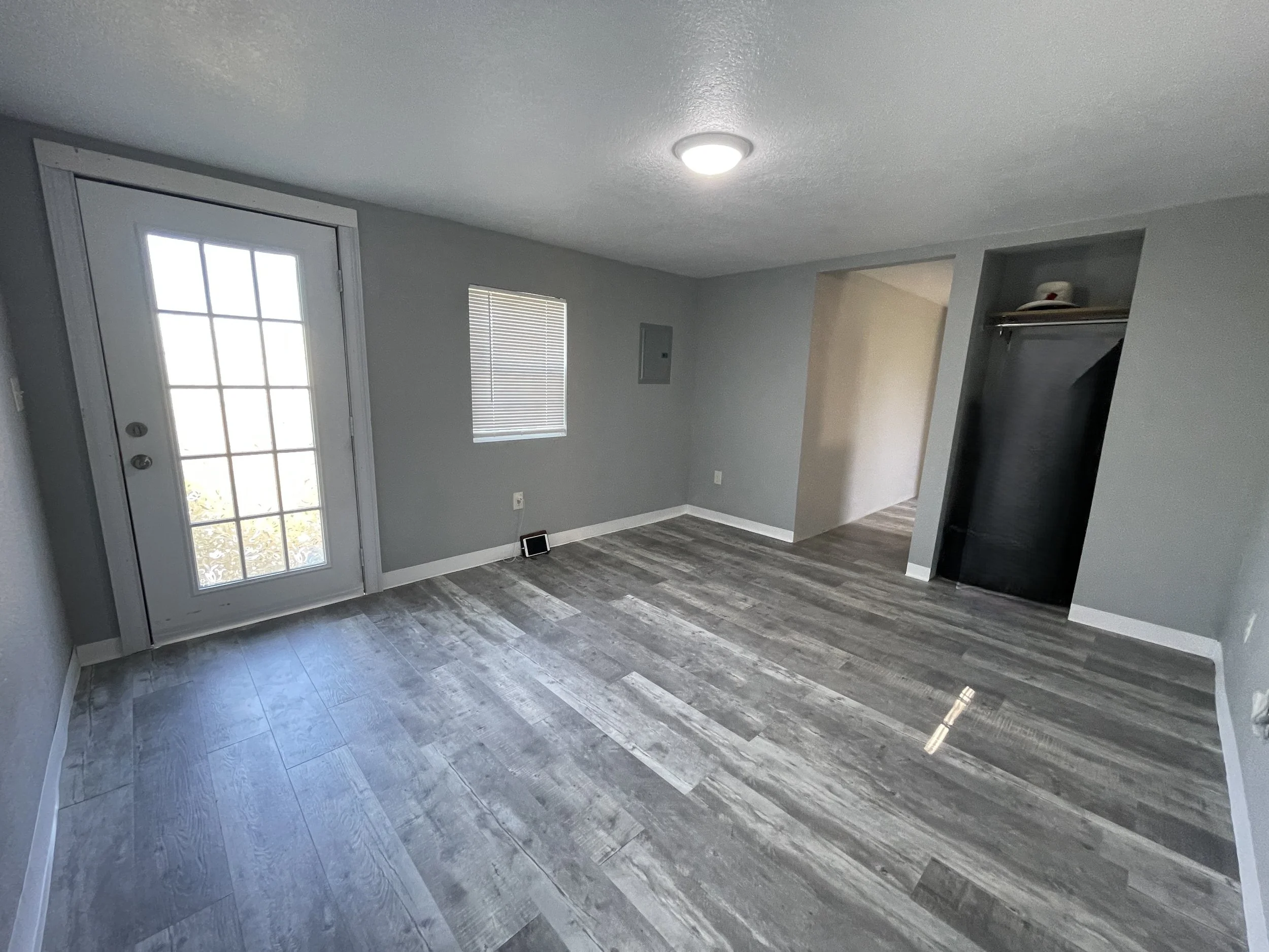 Spacious studio rental room with a dedicated area for a queen bed, armoire, and recliner. Features a through-window heating and cooling unit and an open closet nook.