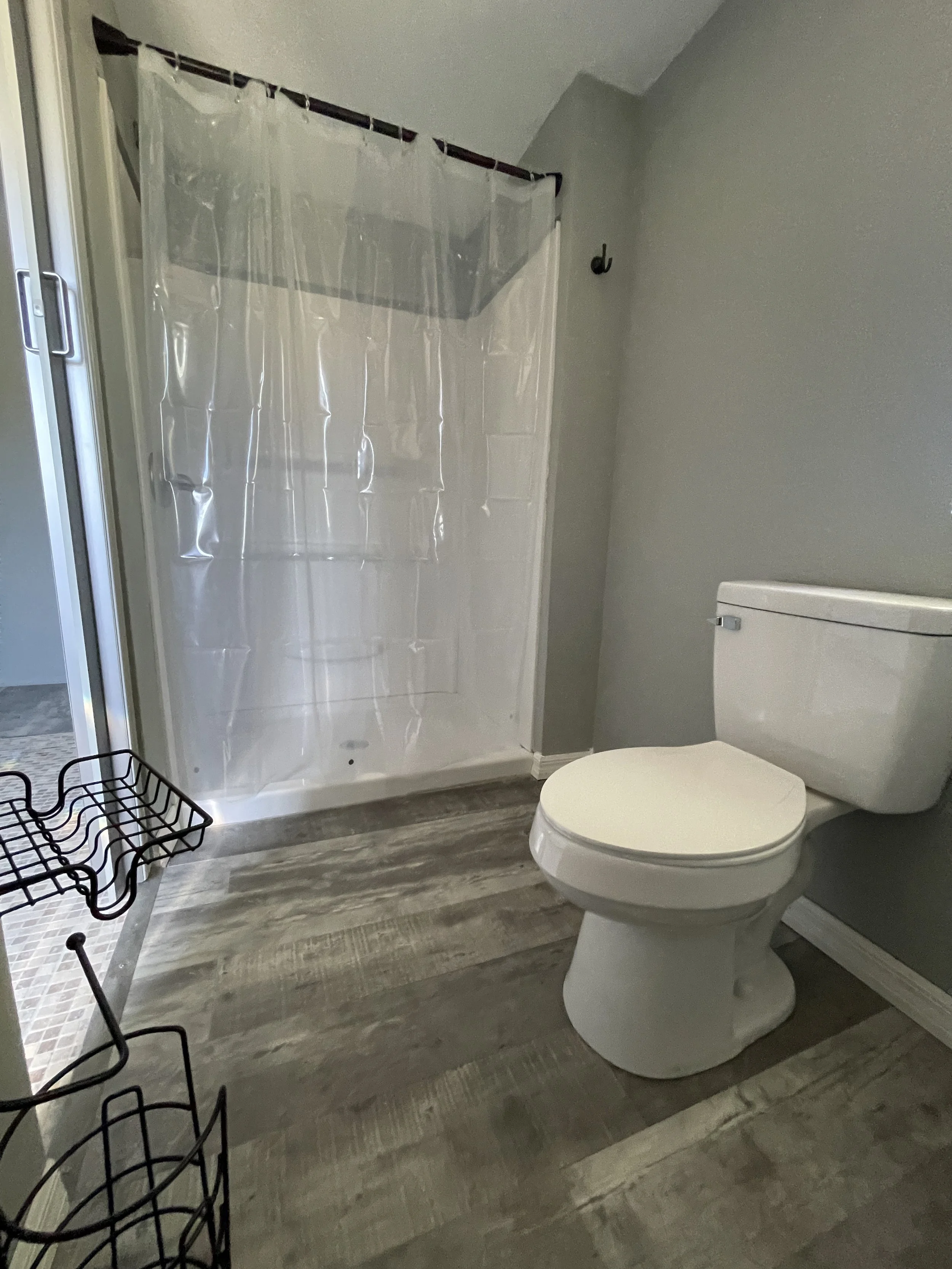 Bathroom interior of a studio rental featuring a large stand-up shower, toilet, and a small narrow frosted window for natural light and privacy.