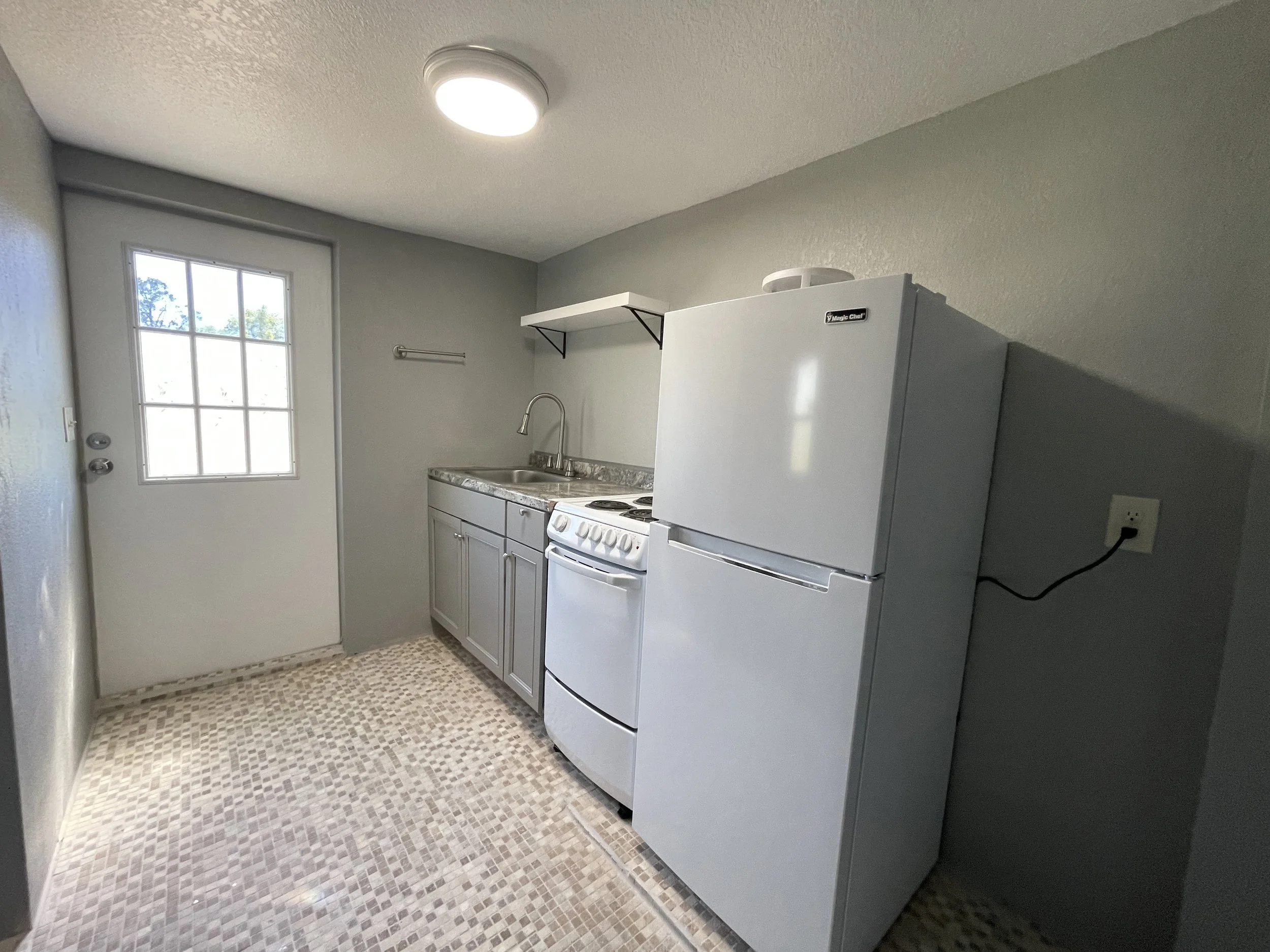 View of the studio's main entrance door adjacent to a space-saving, one-wall kitchenette designed for efficiency and convenience.