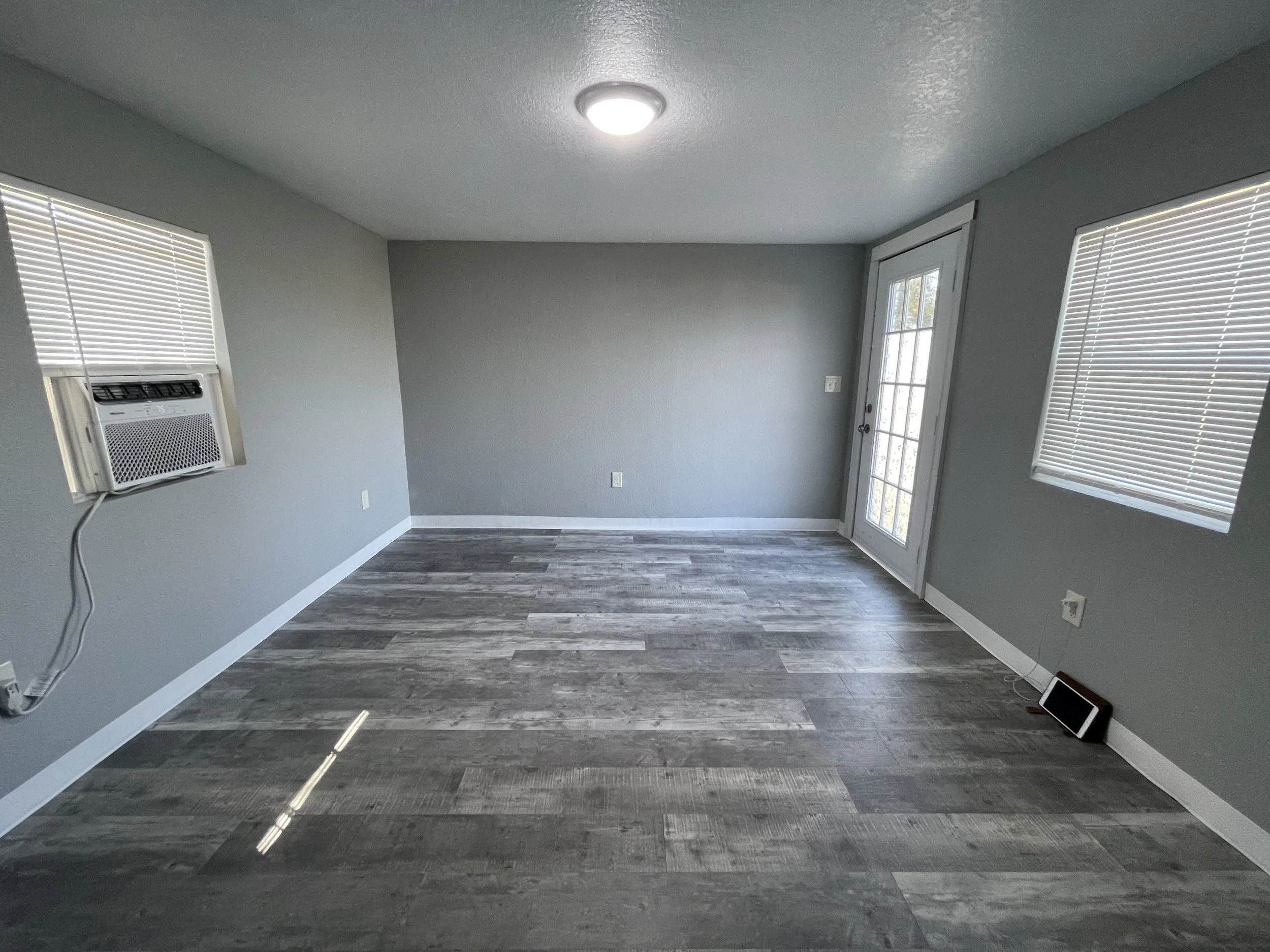 Spacious studio rental room with a dedicated area for a queen bed, armoire, and recliner. Features a through-window heating and cooling unit and an open closet nook.