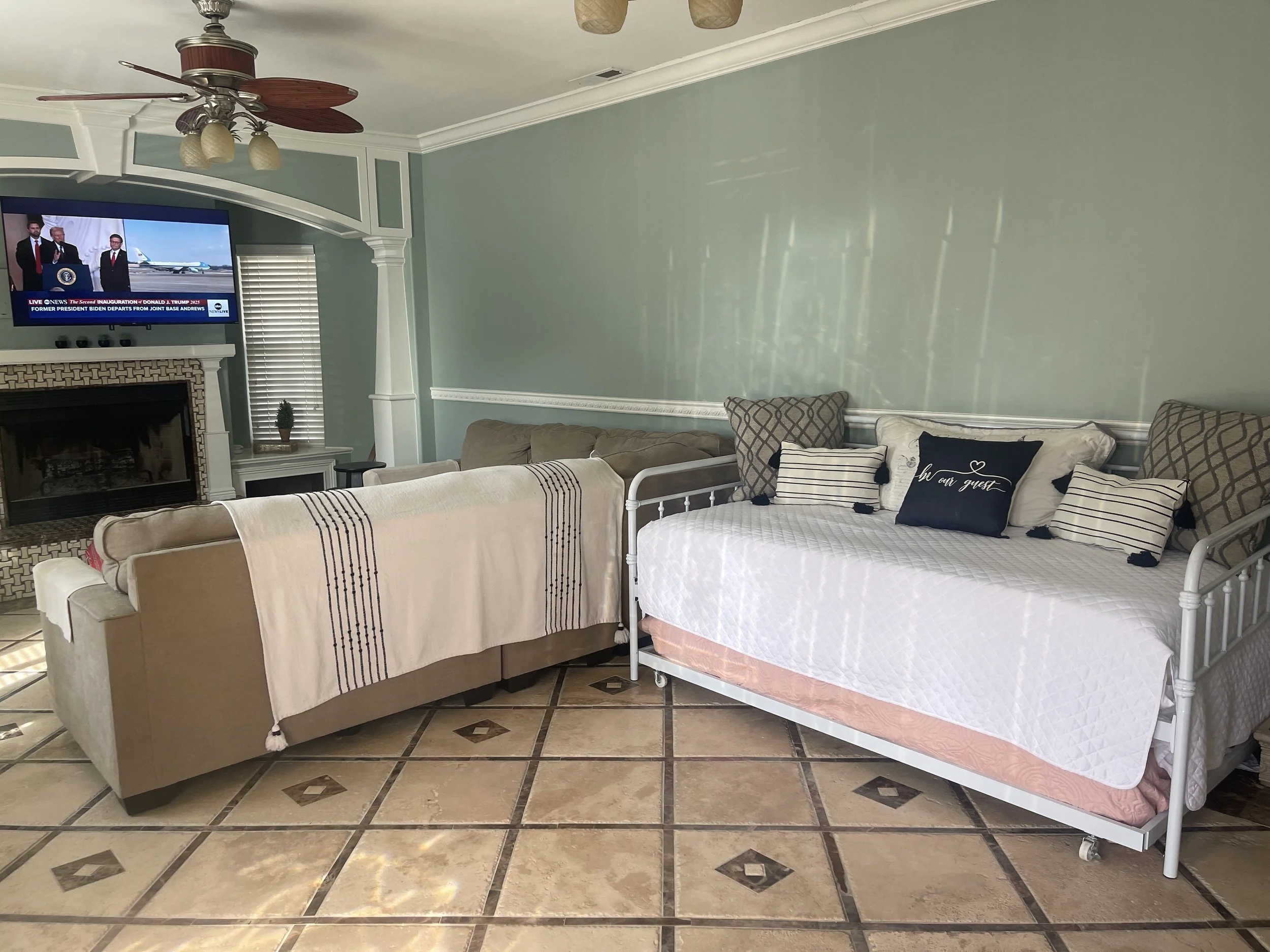 Lake City, FL Airbnb living room featuring a stone wood-burning fireplace, grey L-shaped couch, and a trundle bed for extra guests.