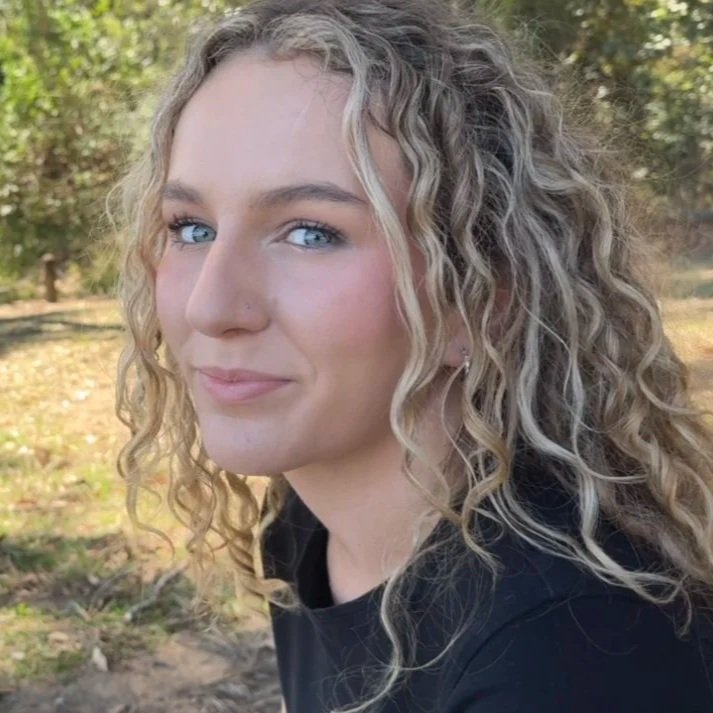 Young woman with curly blonde hair and blue eyes outdoors in a park