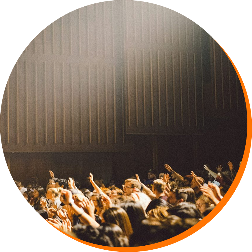 Audience dans une salle de concert ou de théâtre, plusieurs personnes levant les mains.