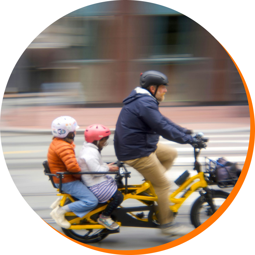 Un homme roulant à vélo avec deux enfants à l'arrière portant des casques.