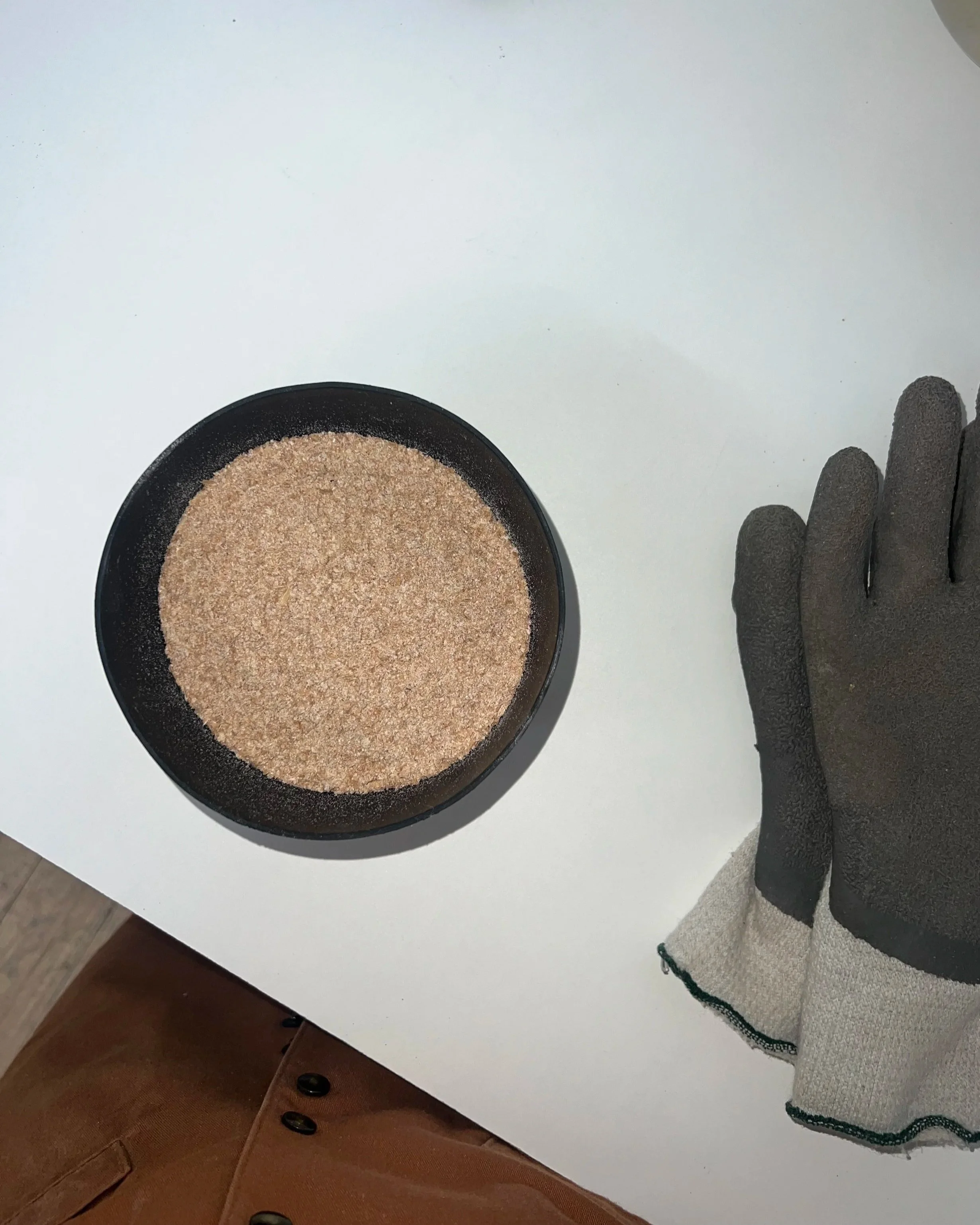 Schwarze Schutzhandschuhe neben einer schwarzen Schüssel mit Sand auf einem weißen Tisch.
