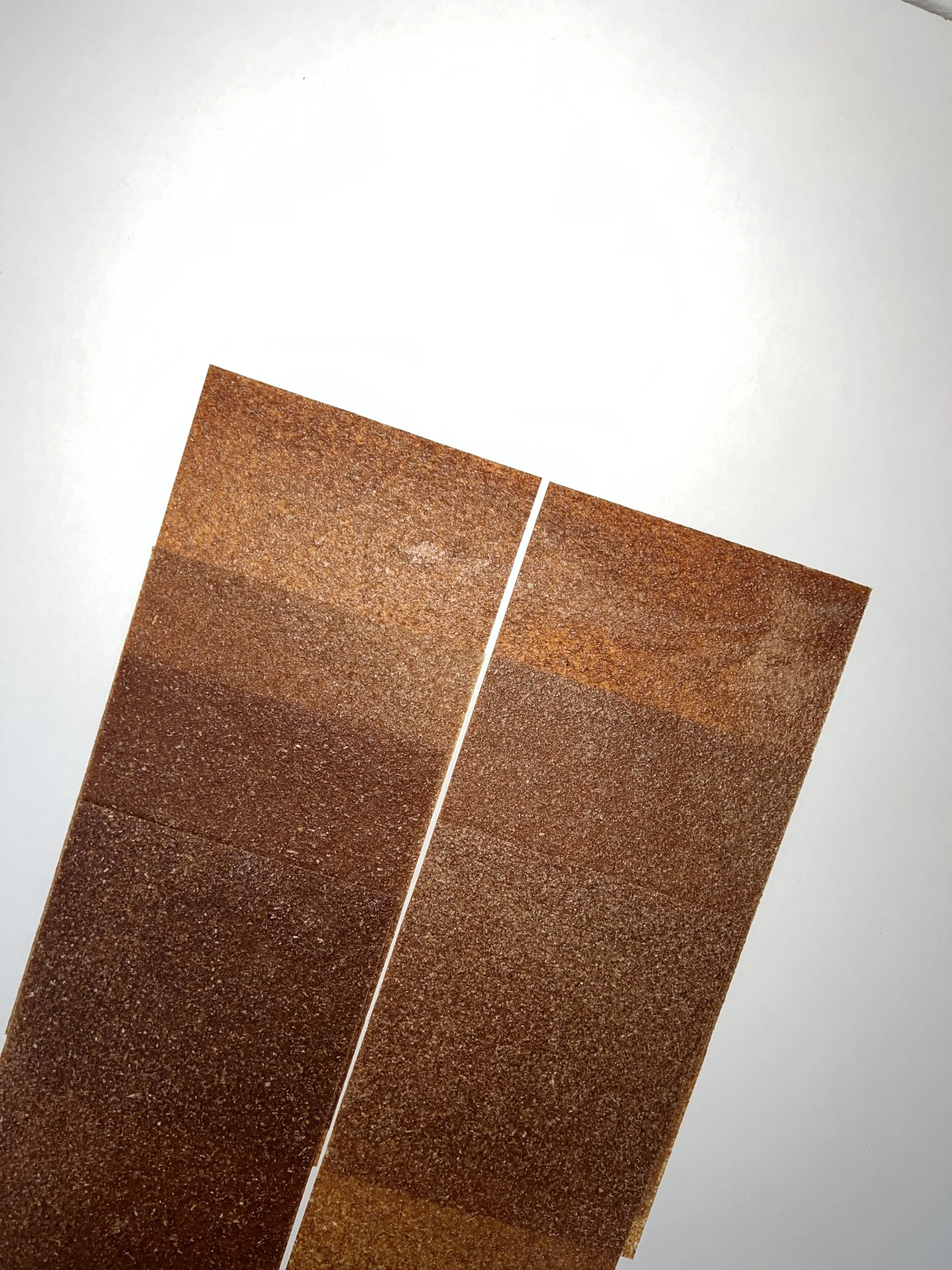 Nahaufnahme von zwei Bahnen mit rotem, sandigem Sandstein-Farbton, die nebeneinander auf einer weißen Oberfläche liegen.