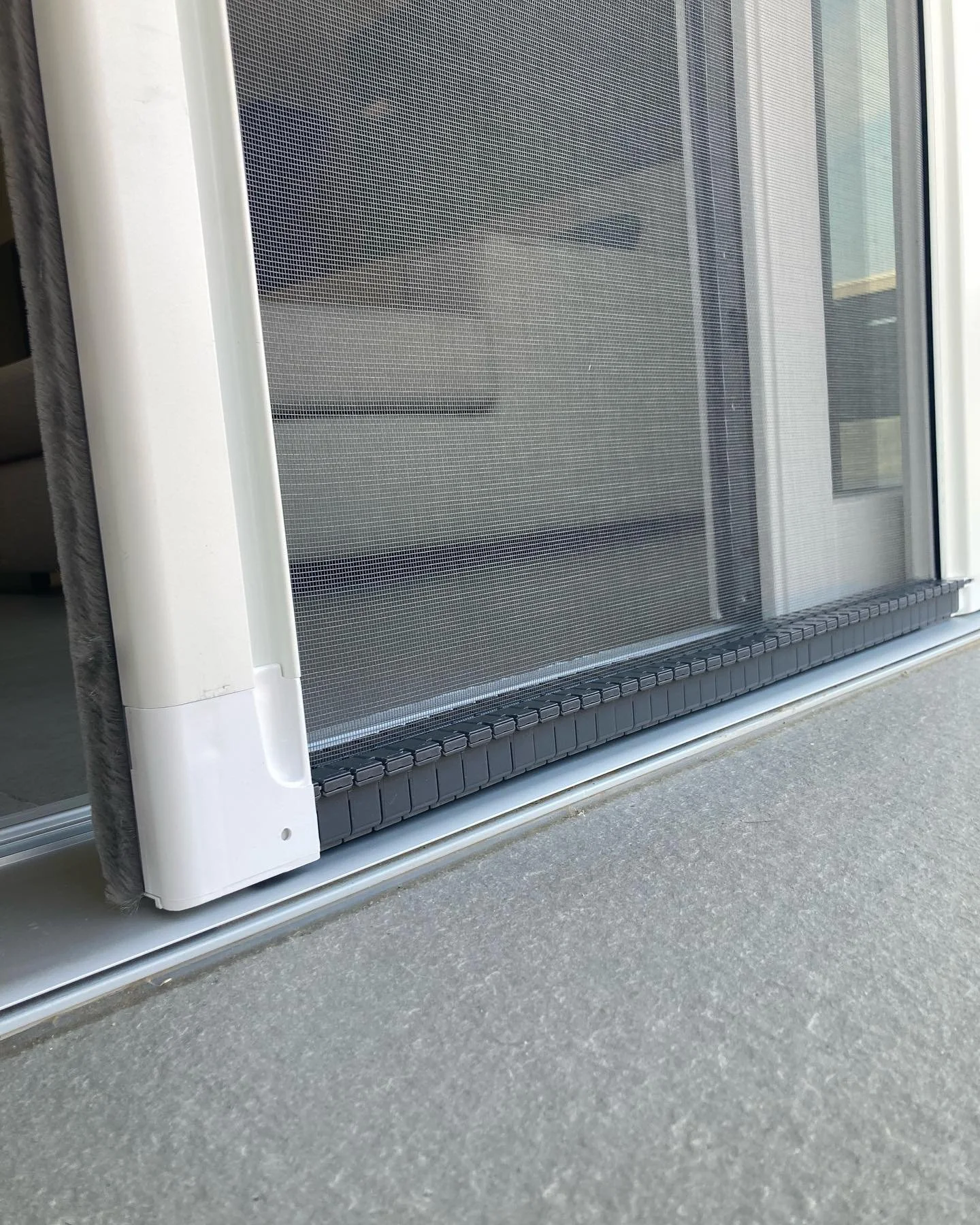 Vista di una finestra con una zanzariera e un condizionatore integrato, con un pavimento in cemento.
