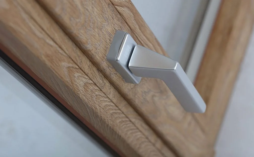 Maniglia della porta in plastica bianca con chiusura a scatto, attaccata a un pannello di legno.