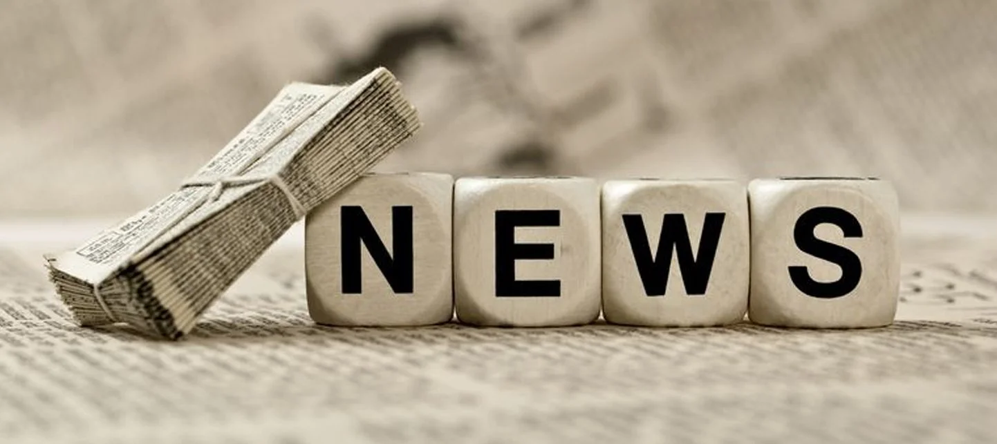 Blocco di lettere che formano la parola 'NEWS', con un rotolino di giornale accanto, su uno sfondo di carta riciclata.