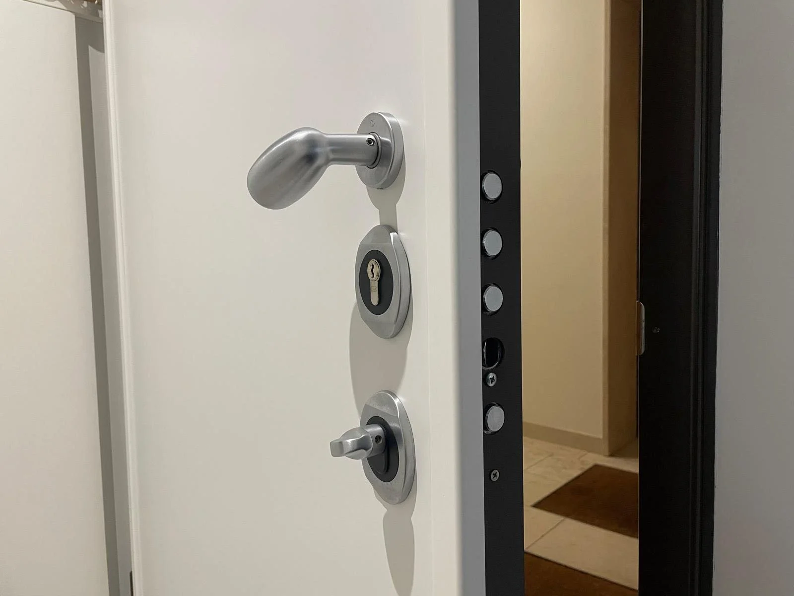 Porta bianca con maniglia in metallo, cilindro per la serratura e chiave, parte della serratura e area di apertura con battente e cilindro in ottone, vista dall'angolazione