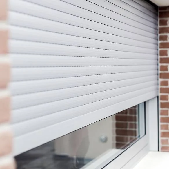 Finestra con persiana avvolgibile bianca parzialmente abbassata, su una parete di mattoni