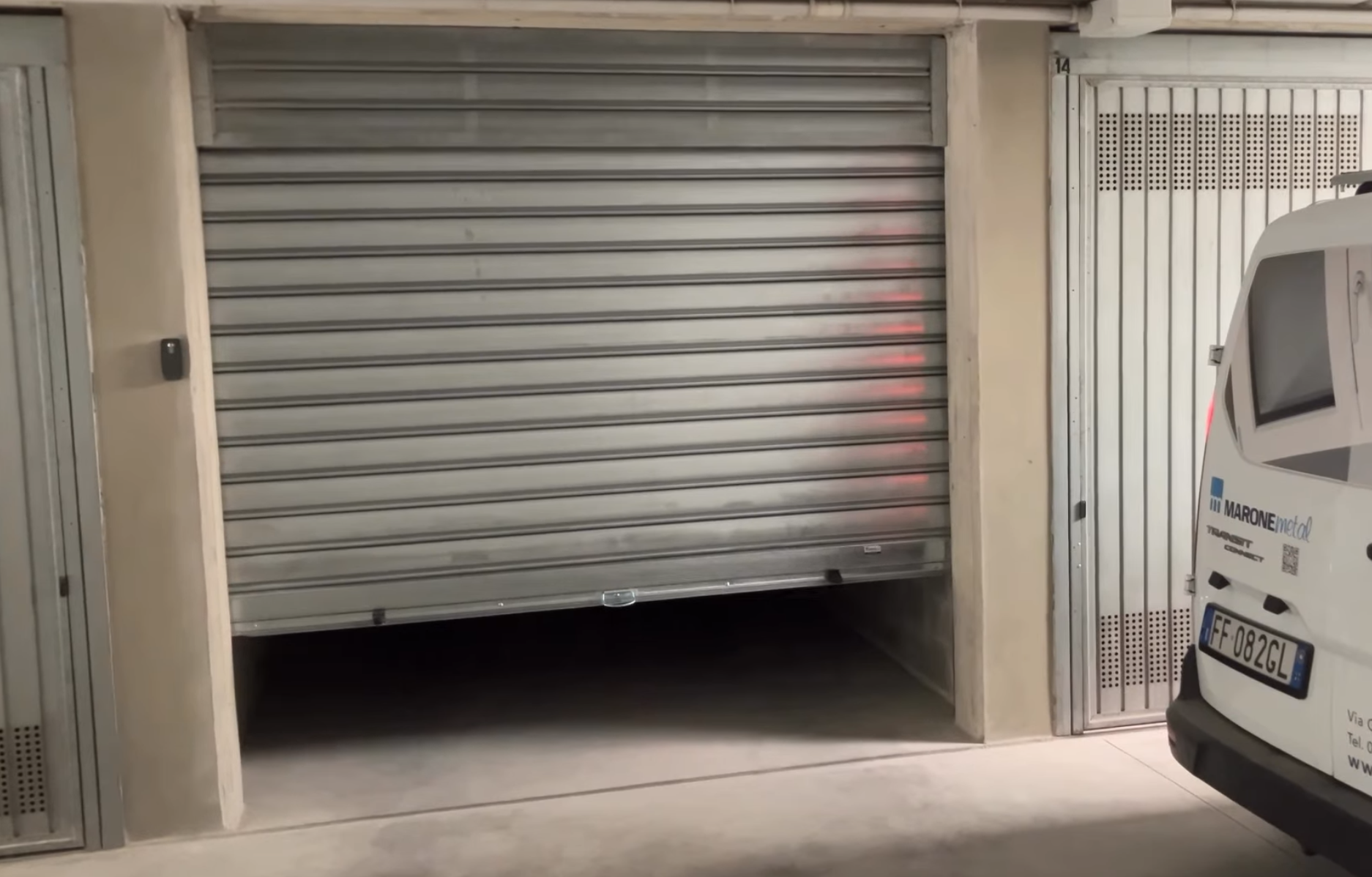 Garage con serranda chiusa e spazio aperto sotto, accanto a un veicolo con targhe italiane