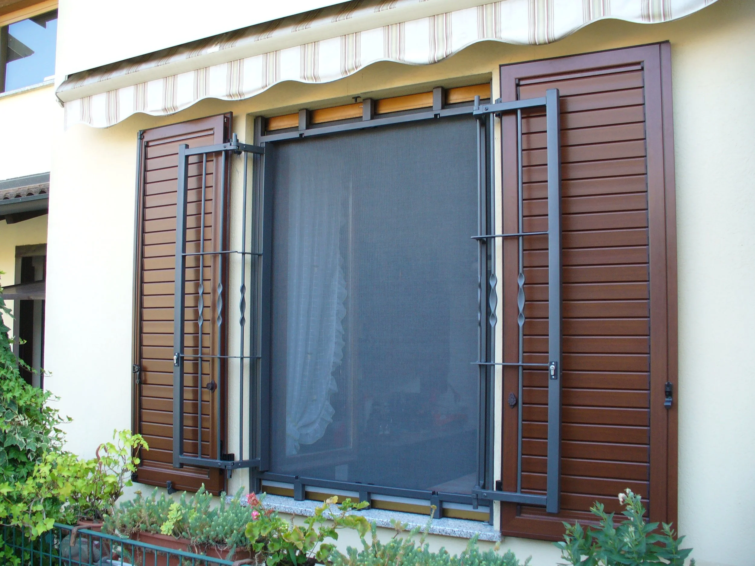 Finestra con tapparella in legno e schermo protettivo, con piante sul davanzale.