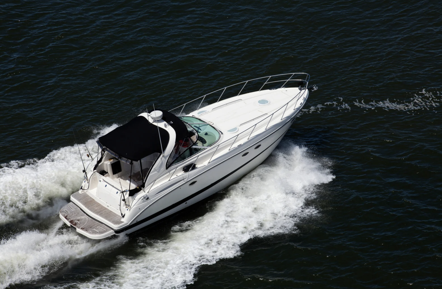 A white motor yacht boat speeding through dark water, leaving a wake behind it, with a black canopy covering the cockpit area.