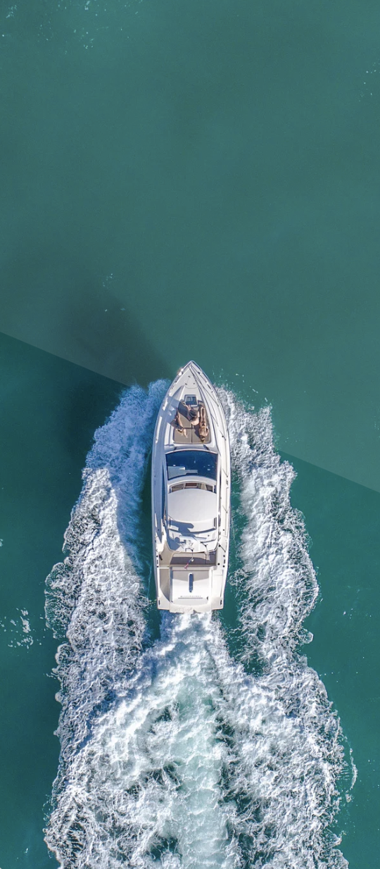 Aerial view of a white speedboat moving across teal water, creating a wake behind it with splashing foam.