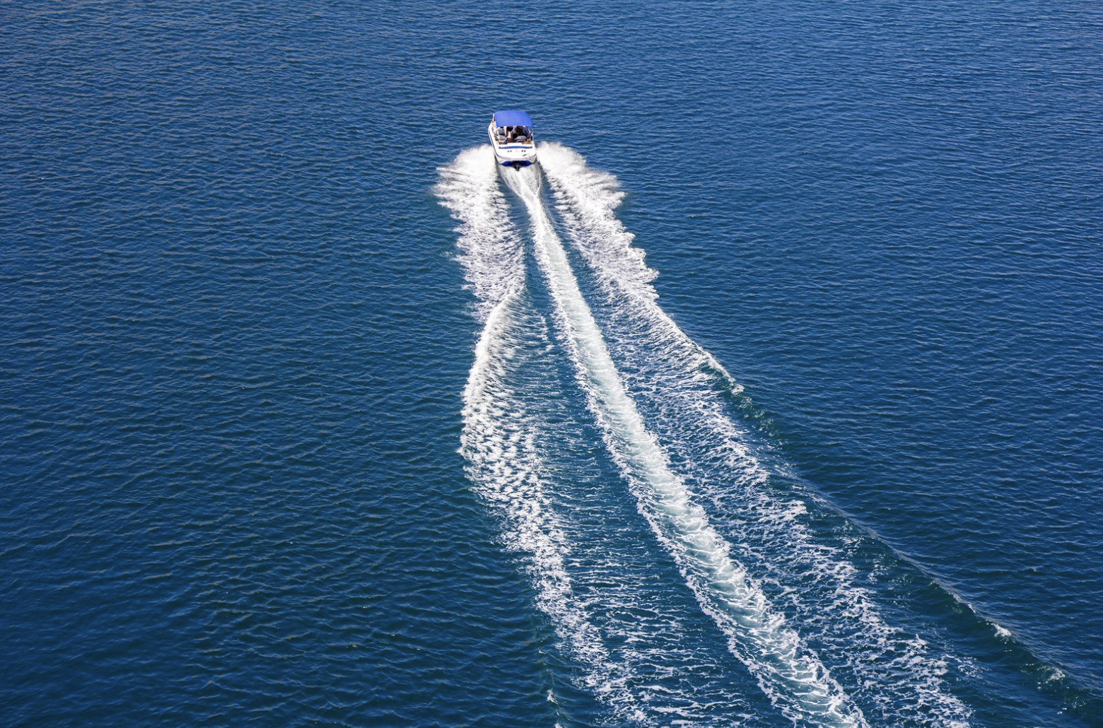 A motorboat speeds across a body of water, creating white foamy wakes behind it.