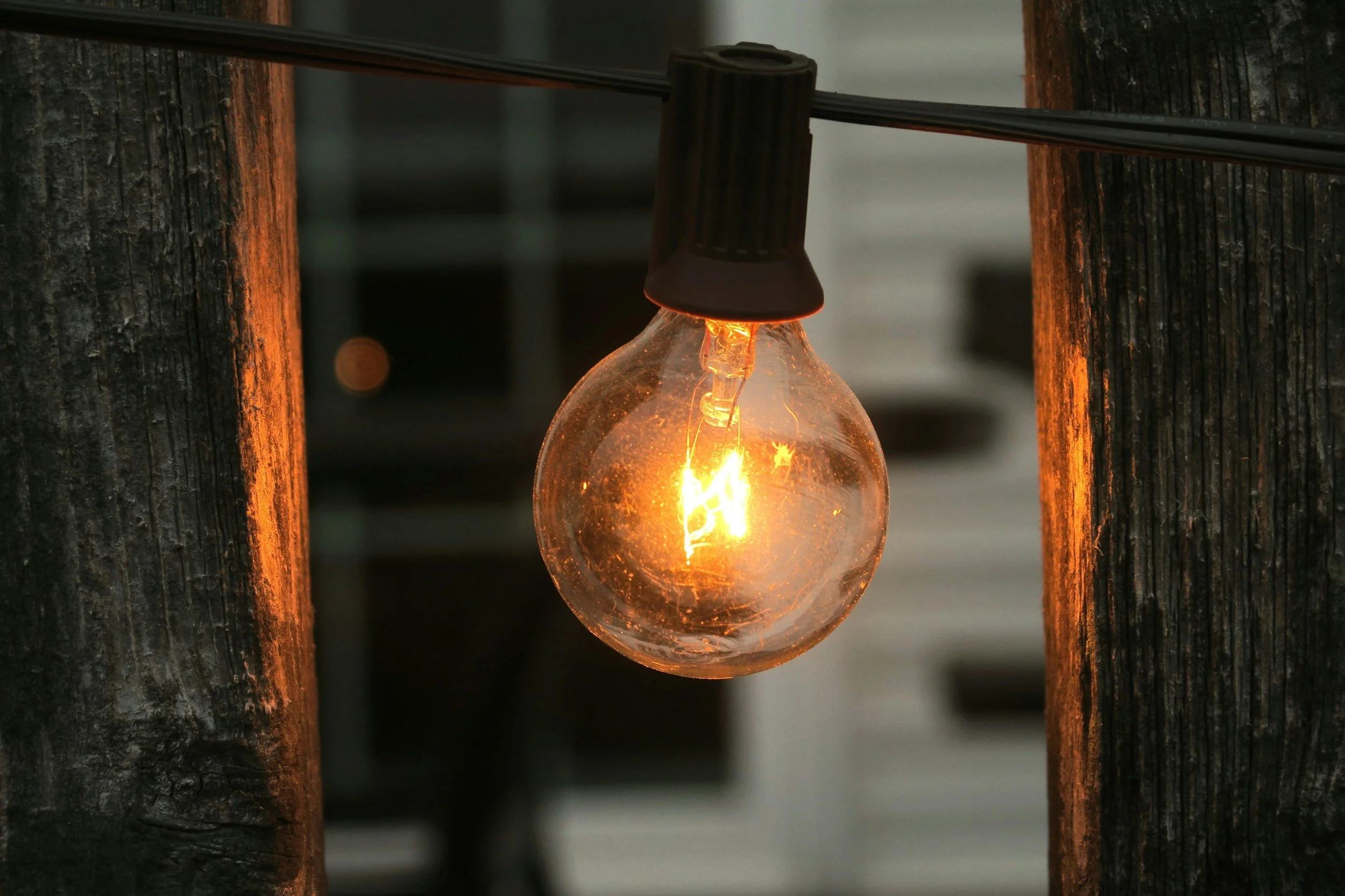 A glowing incandescent light bulb hanging between two weathered wooden posts.