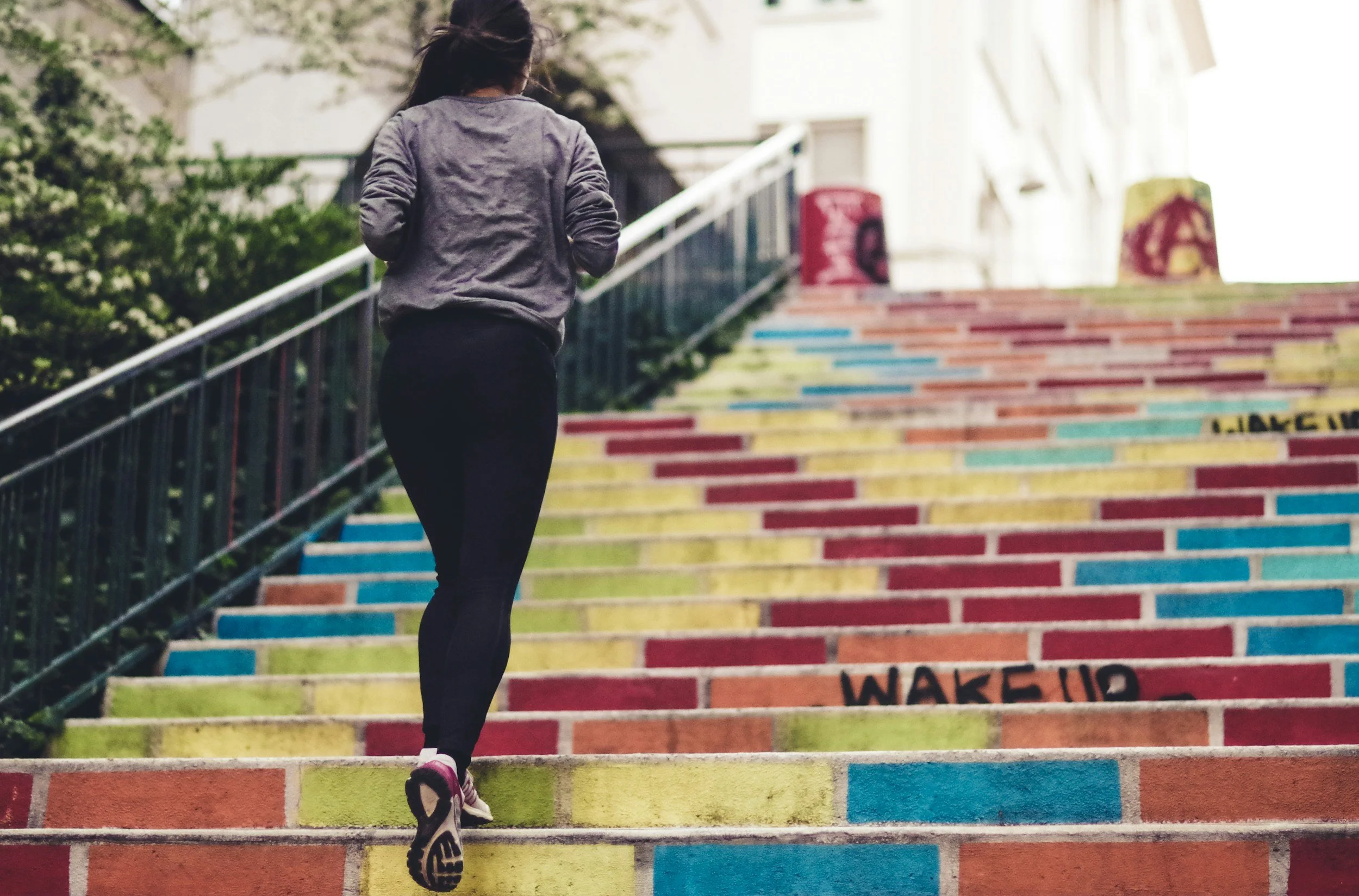 A woman in athletic clothing jogging up colorful painted stairs outdoors.