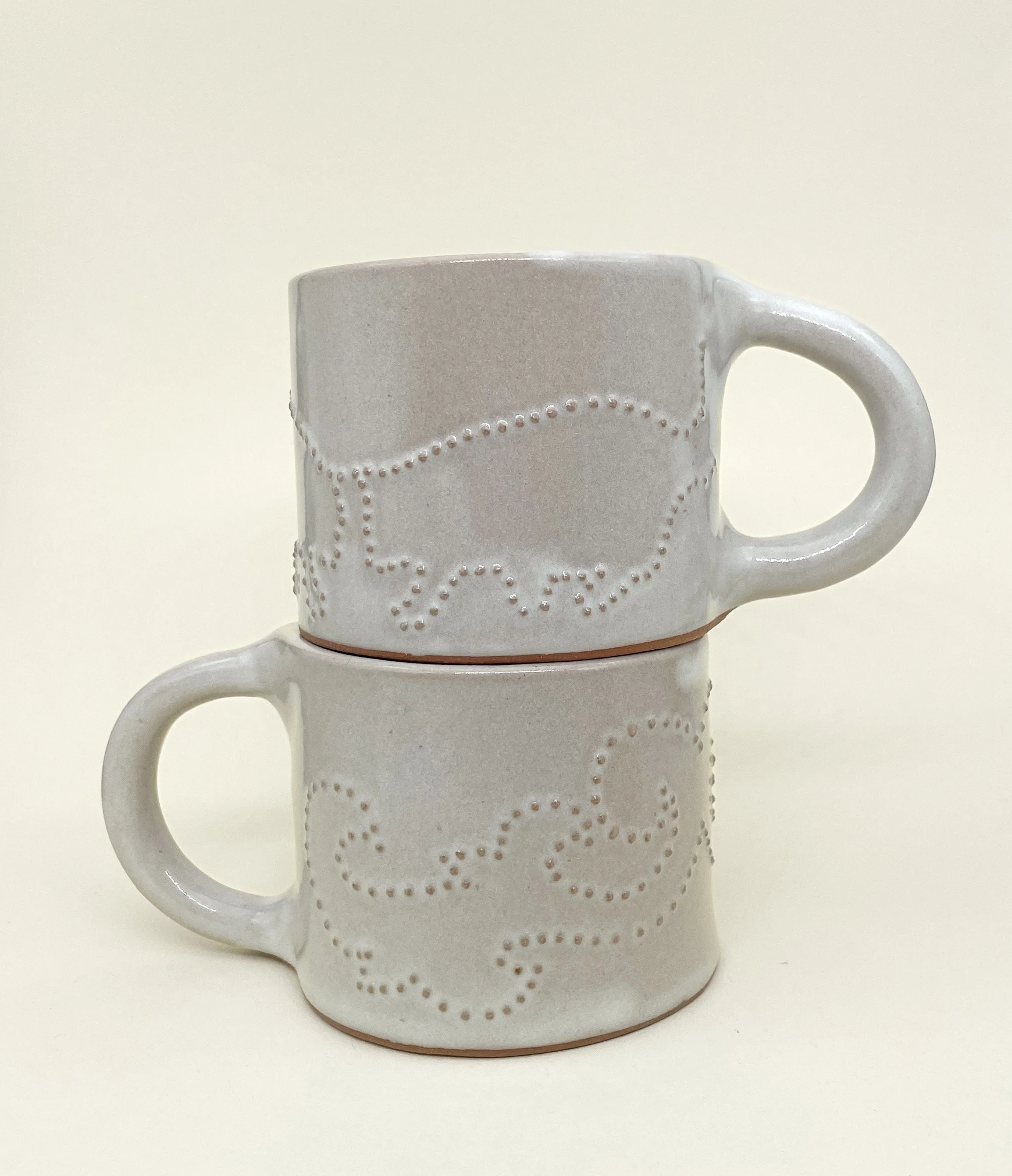 Two stacked white ceramic coffee mugs with dotted decorative patterns on a plain light background.