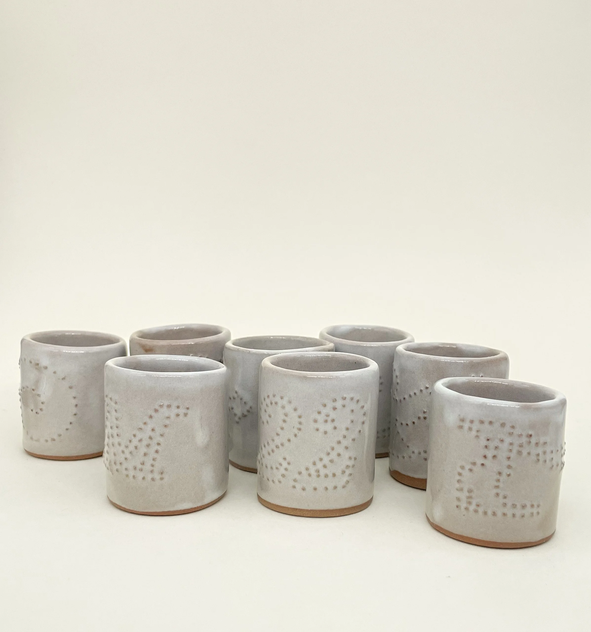 Set of nine white ceramic shot glasses with dotted embossed patterns, arranged in multiple rows on a white background.