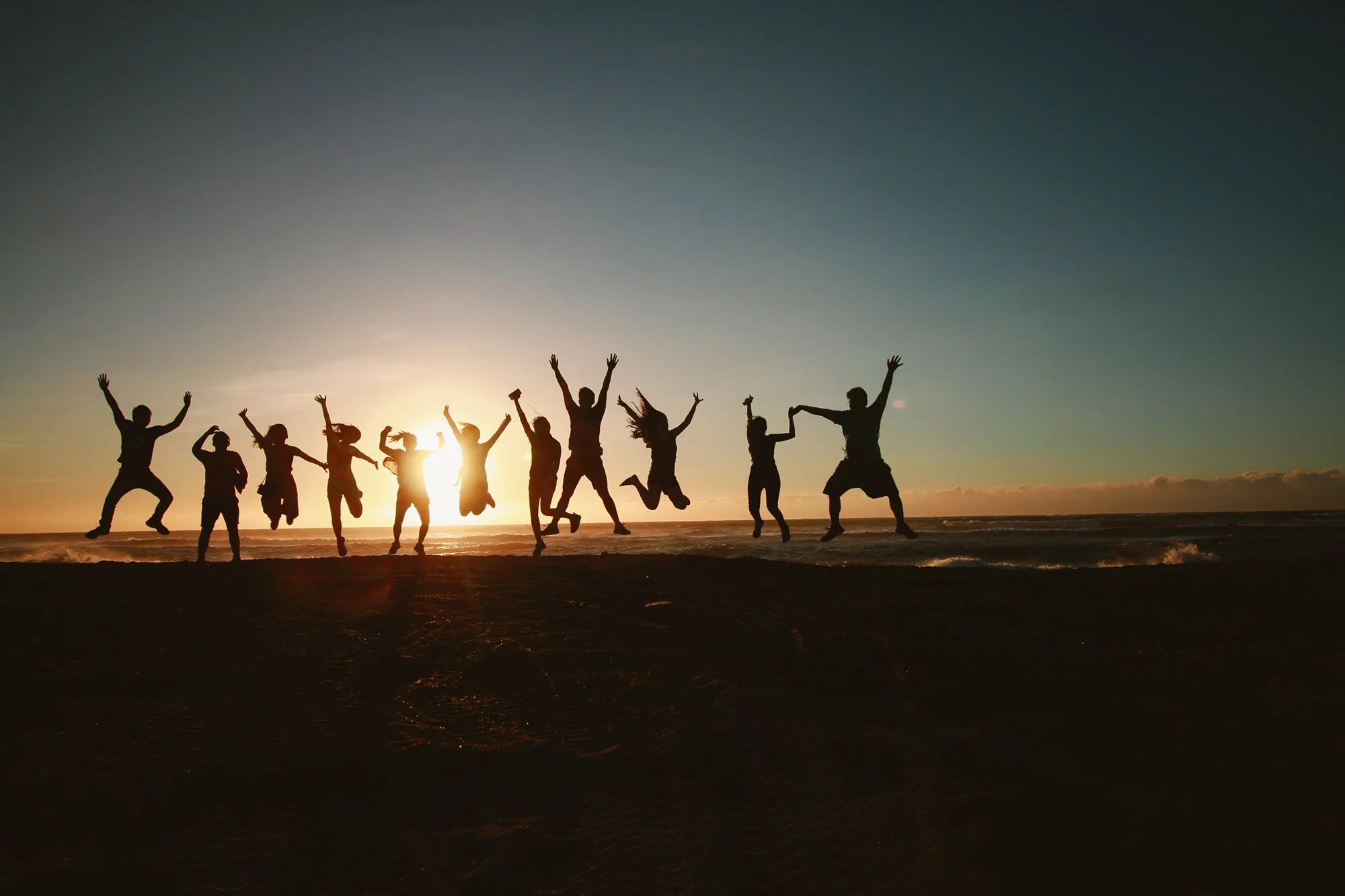 Silhouette of people jumping on a beach at sunset