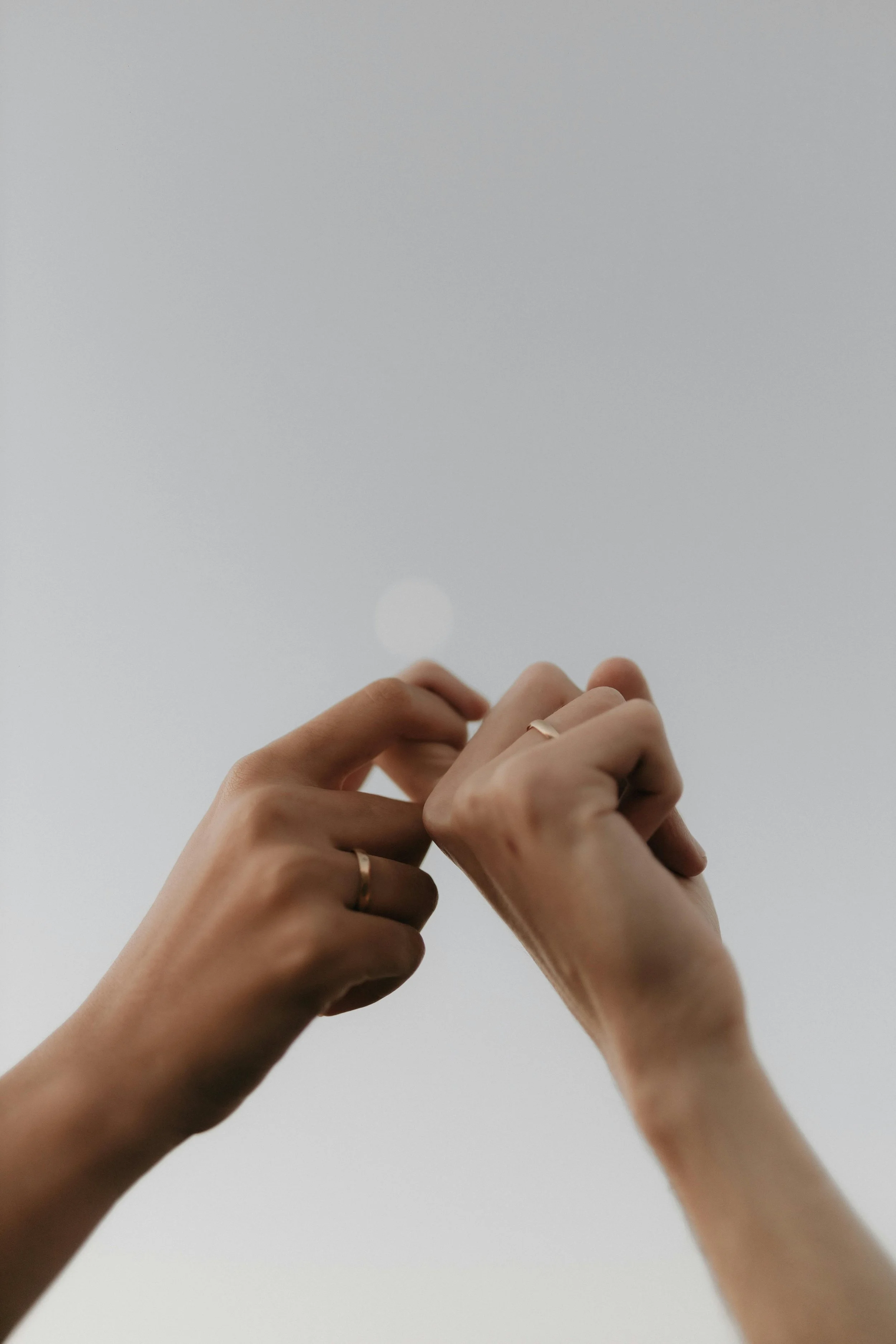 Close-up of two hands with rings, interlocking fingers against a plain, gray background, couple, therapy, marriage, struggle.