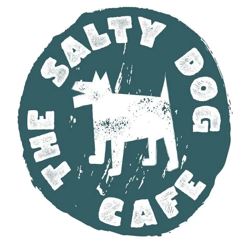 A distressed circular logo with a stylized white moose in the center and the words "THE SAFETY DOG CAFE" around the edge, all in white on a dark background.