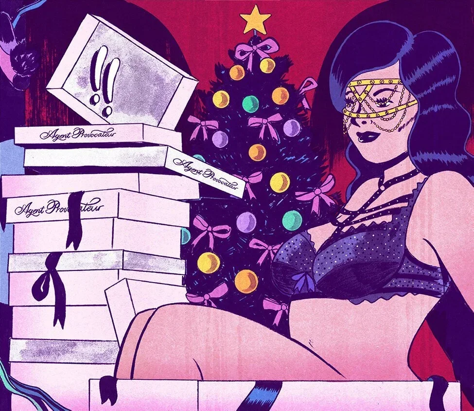 A woman in lingerie with dark hair, wearing gold glasses and chained jewelry, sitting next to a decorated Christmas tree with pink bows and multicolored ornaments, surrounded by stacked white boxes labeled "Agent Provocateur" and marked with exclamat