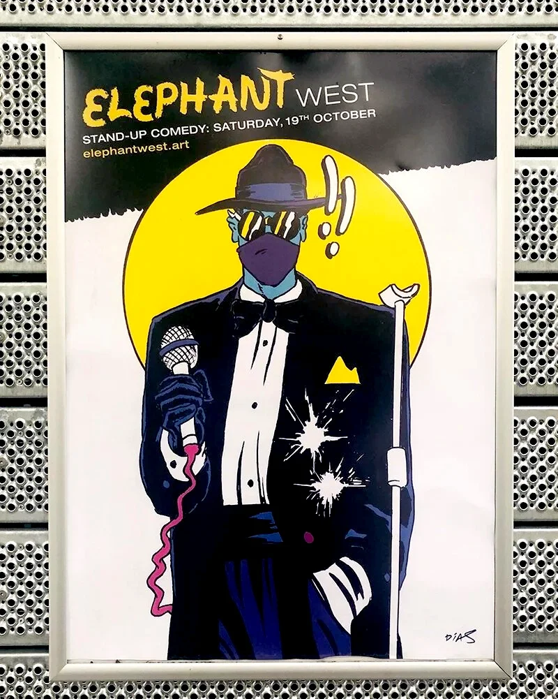 A poster for Elephant West comedy show, featuring a stylized illustration of a person in a tuxedo with flair, wearing a fedora, sunglasses, and a face mask, holding a microphone and a cane, with a yellow circle background.