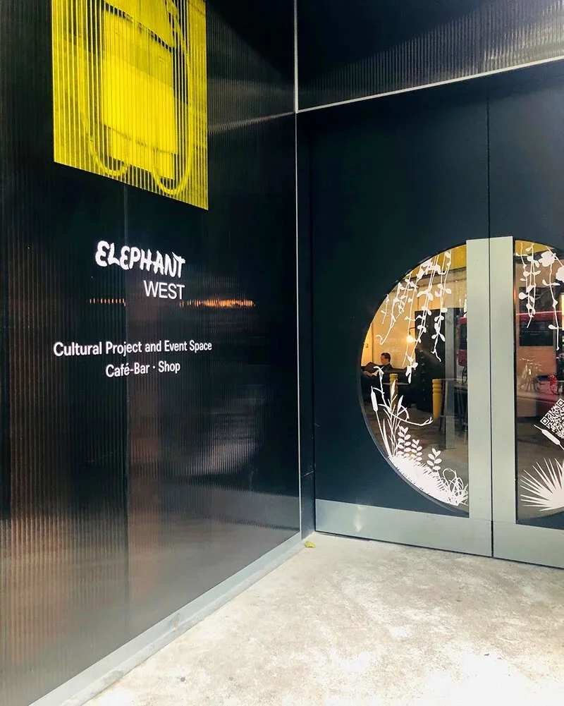 Entrance to Elephant West, a cultural project and event space with a café, bar, and shop, featuring black walls and a decorative circular window with floral patterns.