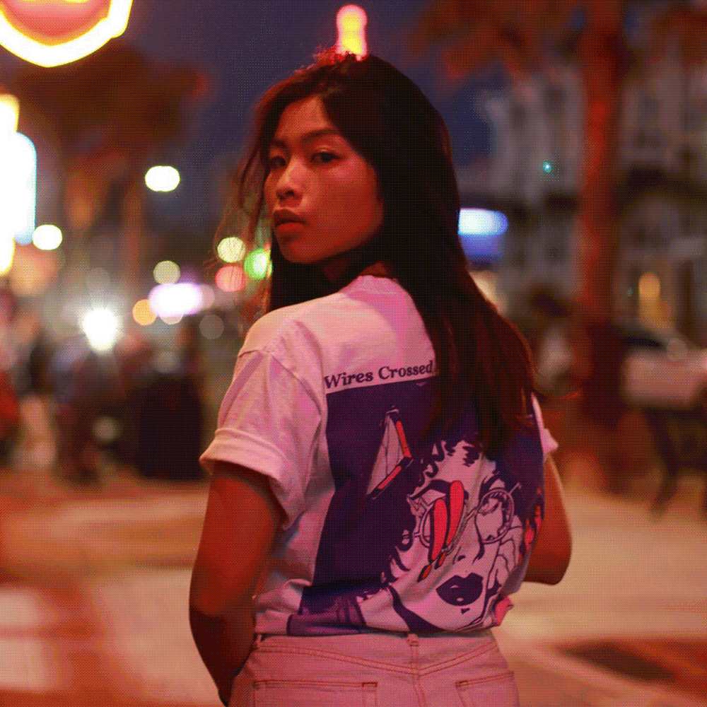 A woman with long black hair looking over her shoulder at night in an urban street, illuminated by colorful city lights and signs.