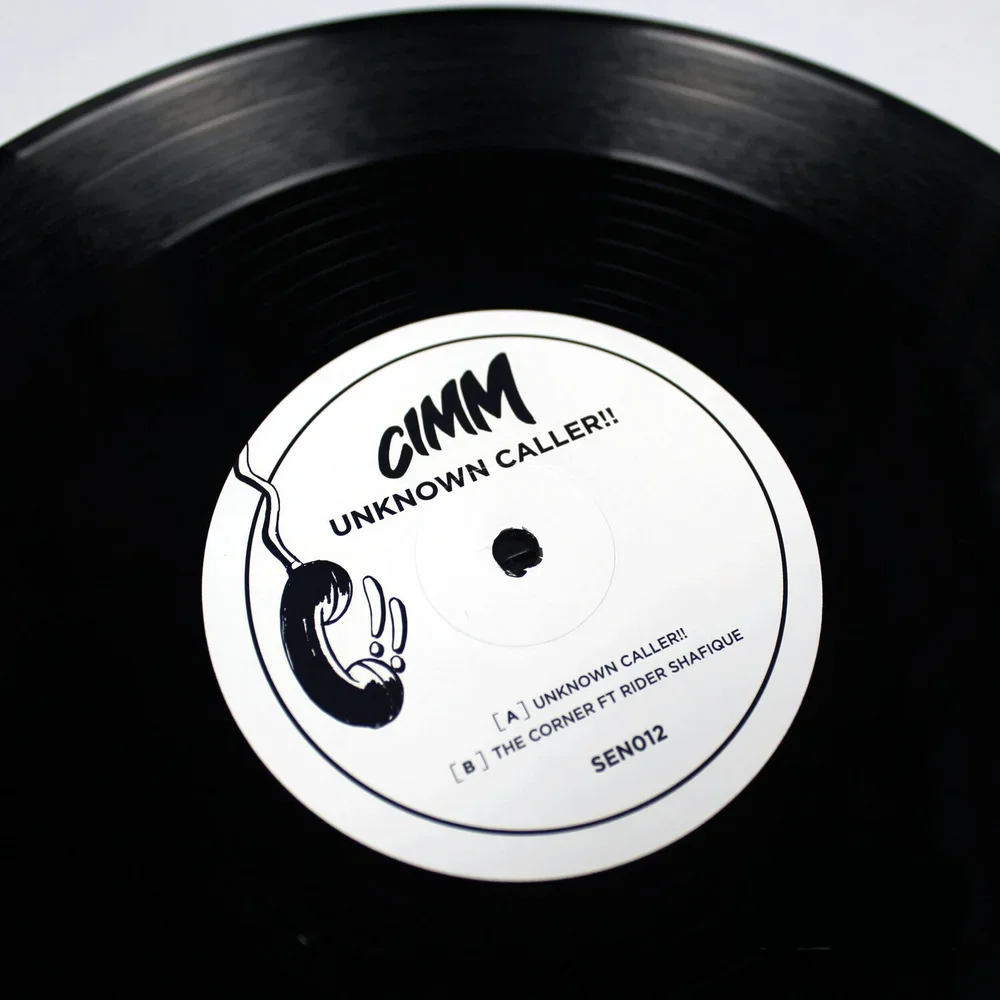 Close-up of a black vinyl record with a white label that has a drawing of a telephone handset and the bold text 'GIMMM'.