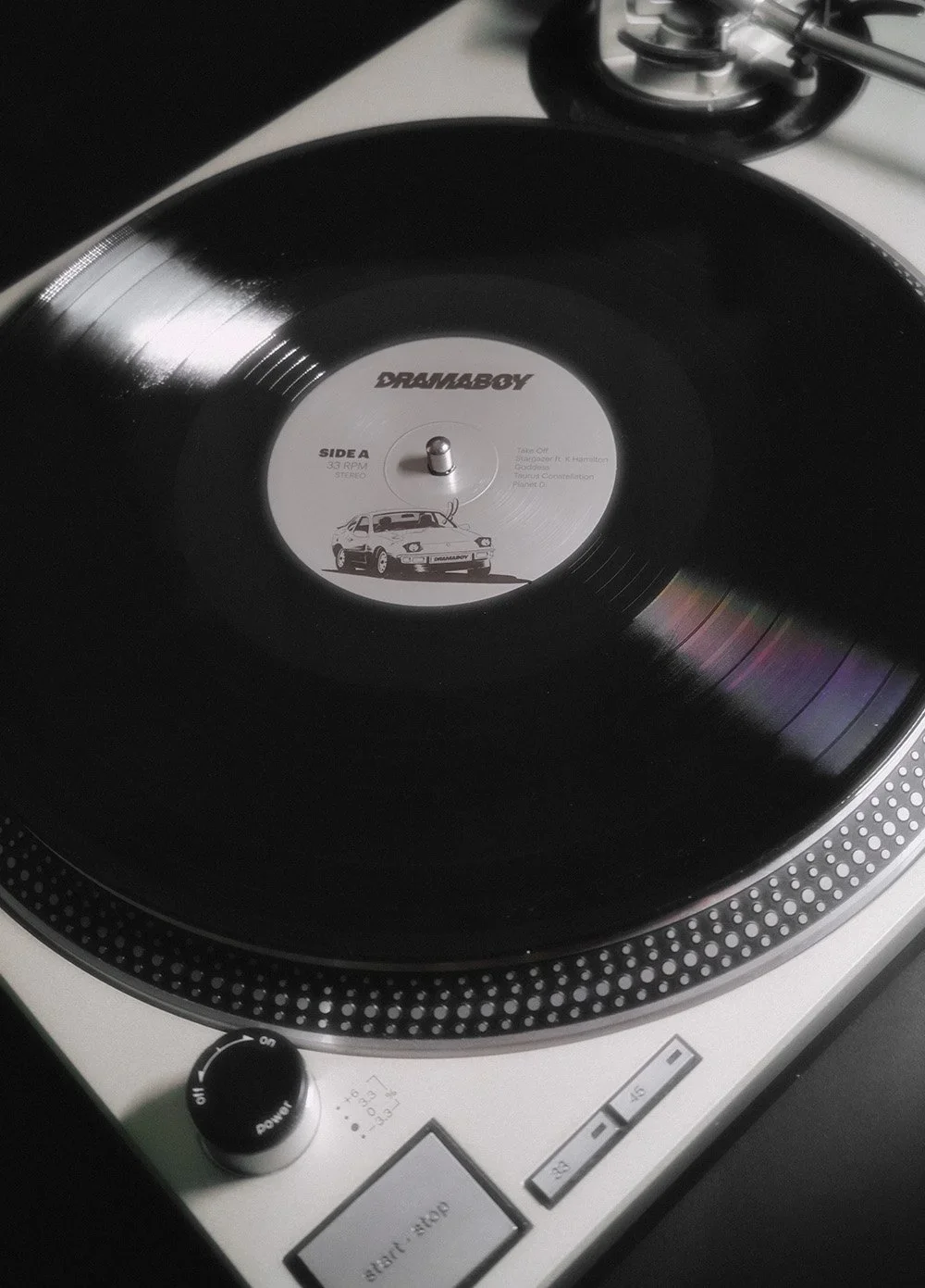 A turntable playing a black vinyl record with a white label that features a car illustration and the label name 'DRAMABOY'.