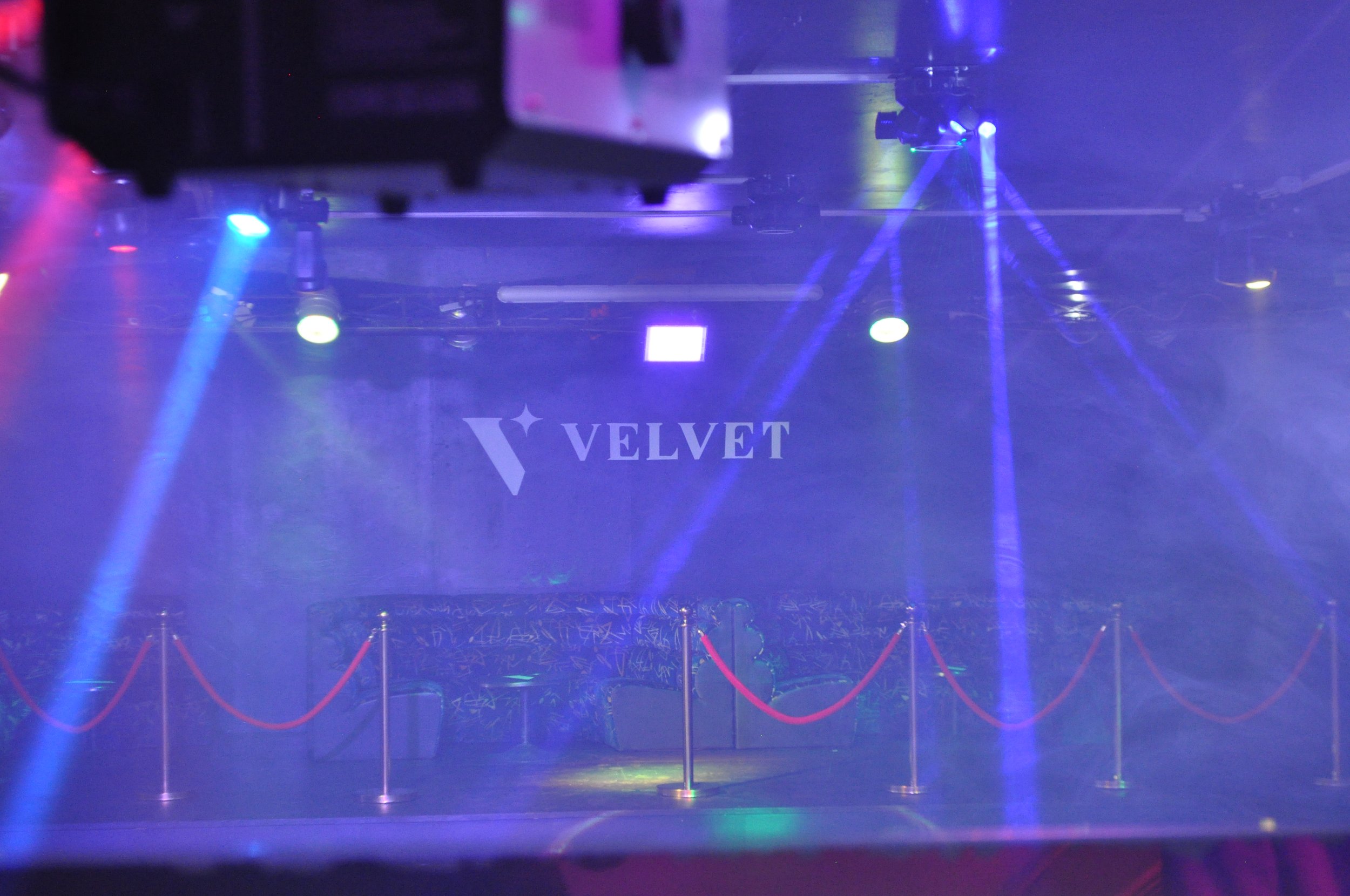 Salle de spectacle avec éclairage violet et bleu, cordons de velours rouge et logo 'Velvet' sur le mur.