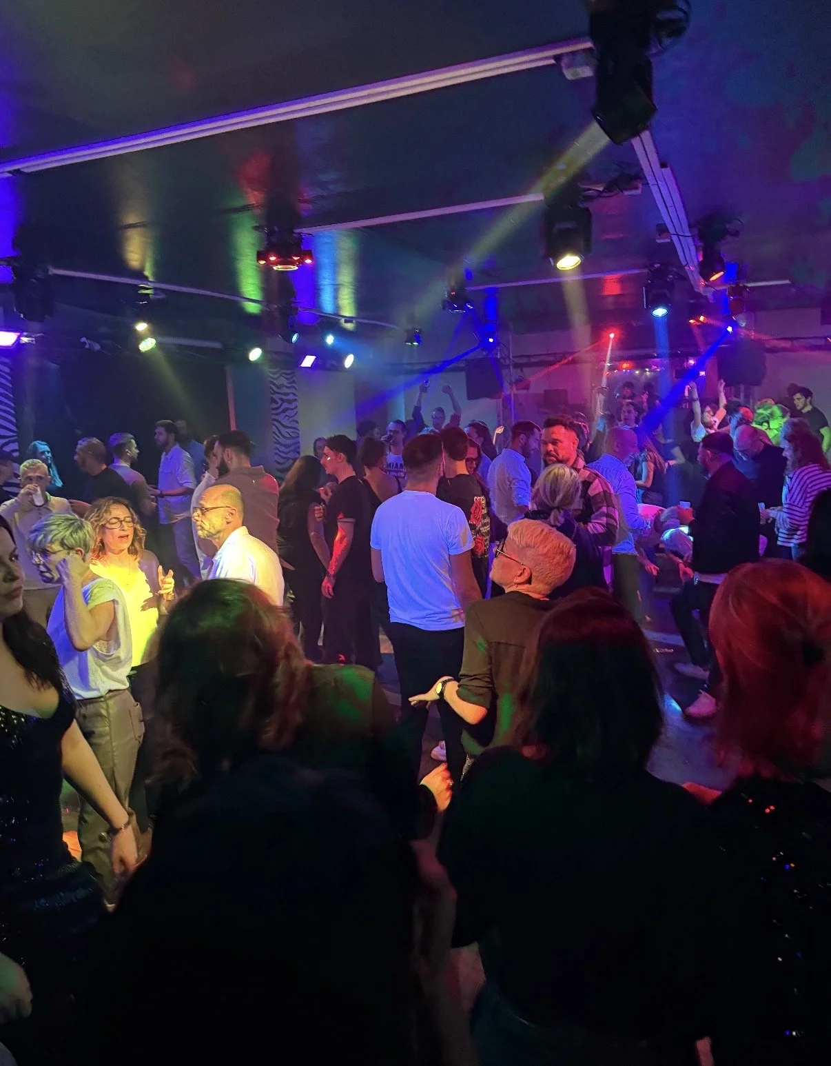 Une salle de danse animée avec de nombreuses personnes qui dansent et socialisent sous un éclairage coloré de discothèque.