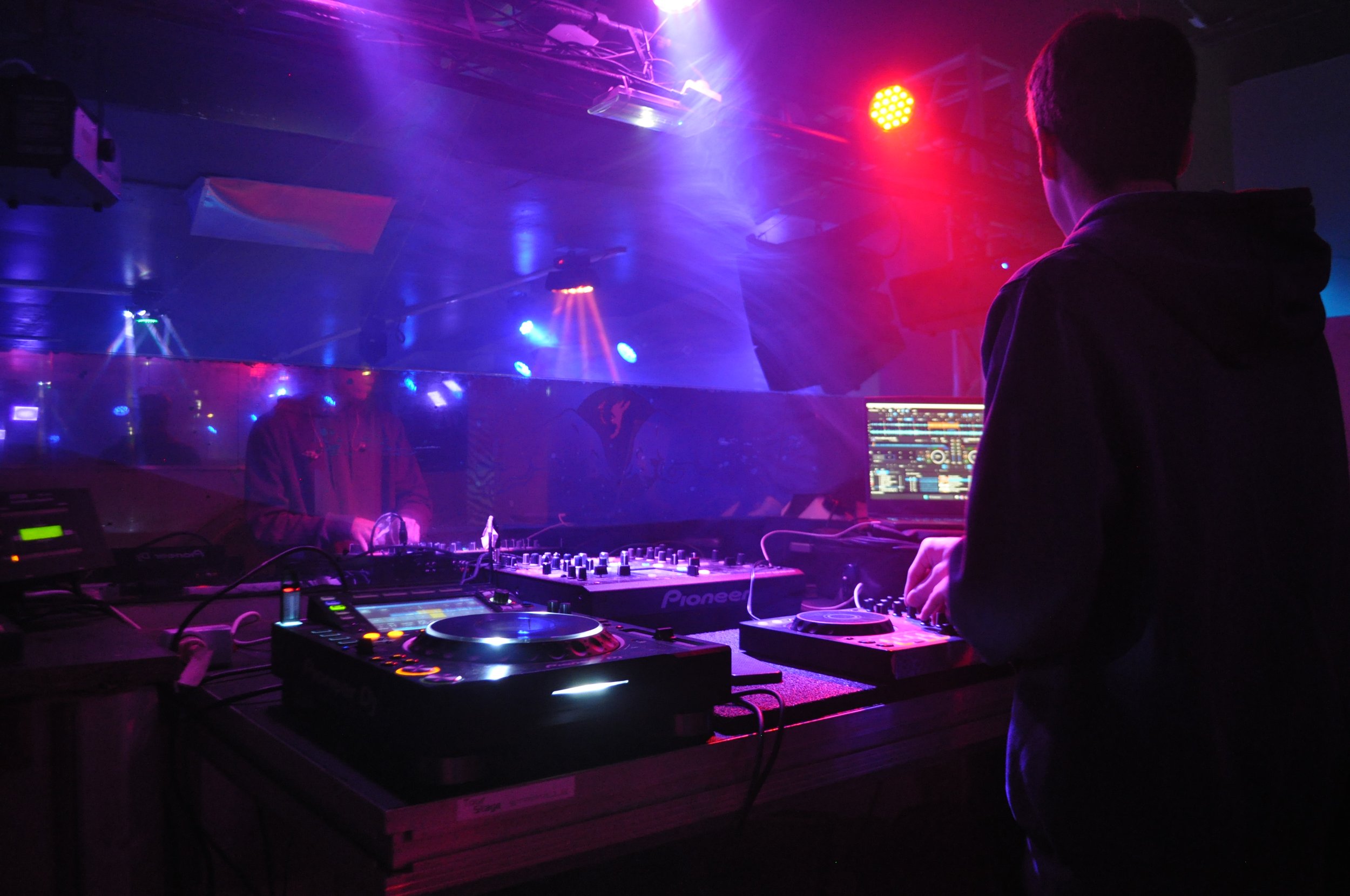 DJ jouant de la musique derrière un plateau avec éclairage de scène violet et rouge dans un club