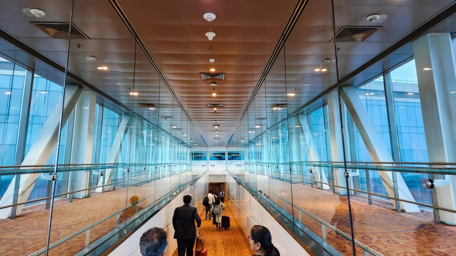 view of walking through an airport with full glass walles on either side and a descending path through to the airport