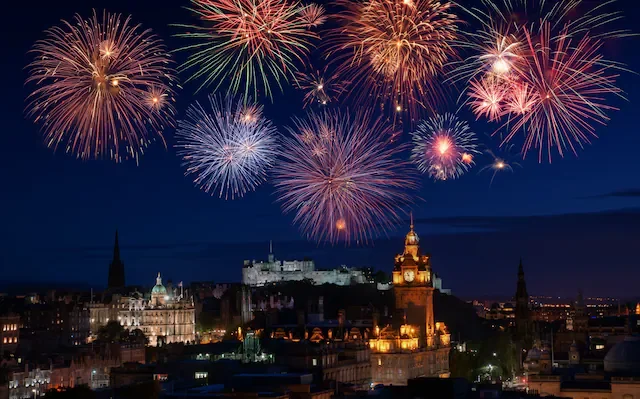 Fireworks light up the night sky over a cityscape with historic buildings and a castle.