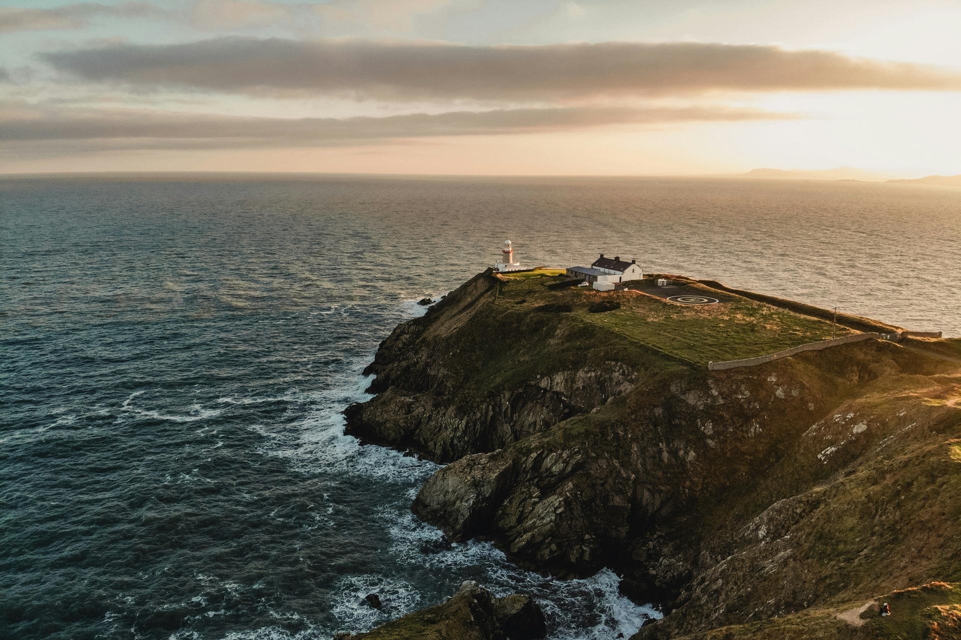 a lighthouse on the edge of a spit of land surrounded by the sea washing up against the cliff faces