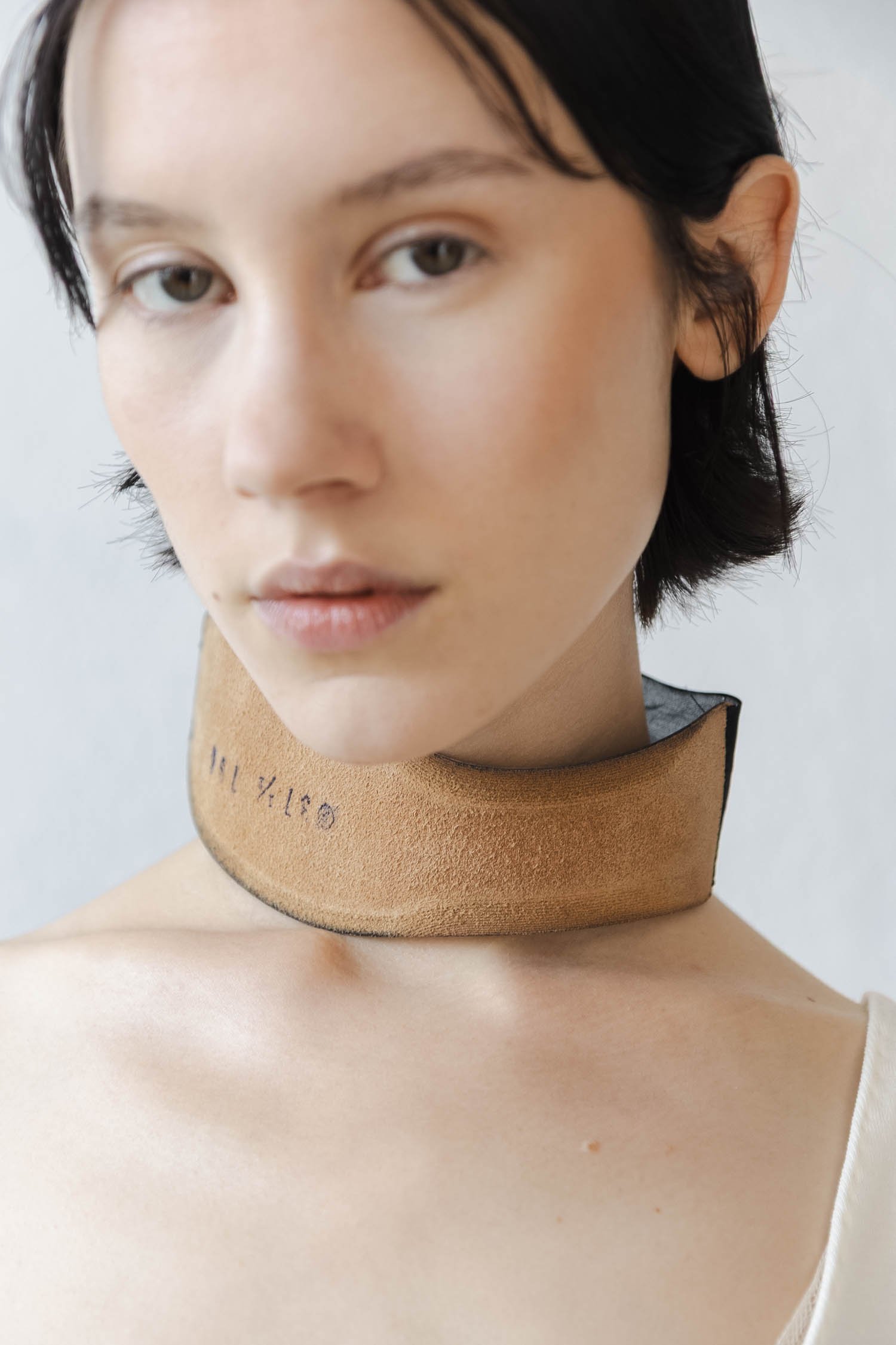 Jeune femme avec un collier en cuir beige portant le texte 'BSTJ 16'.