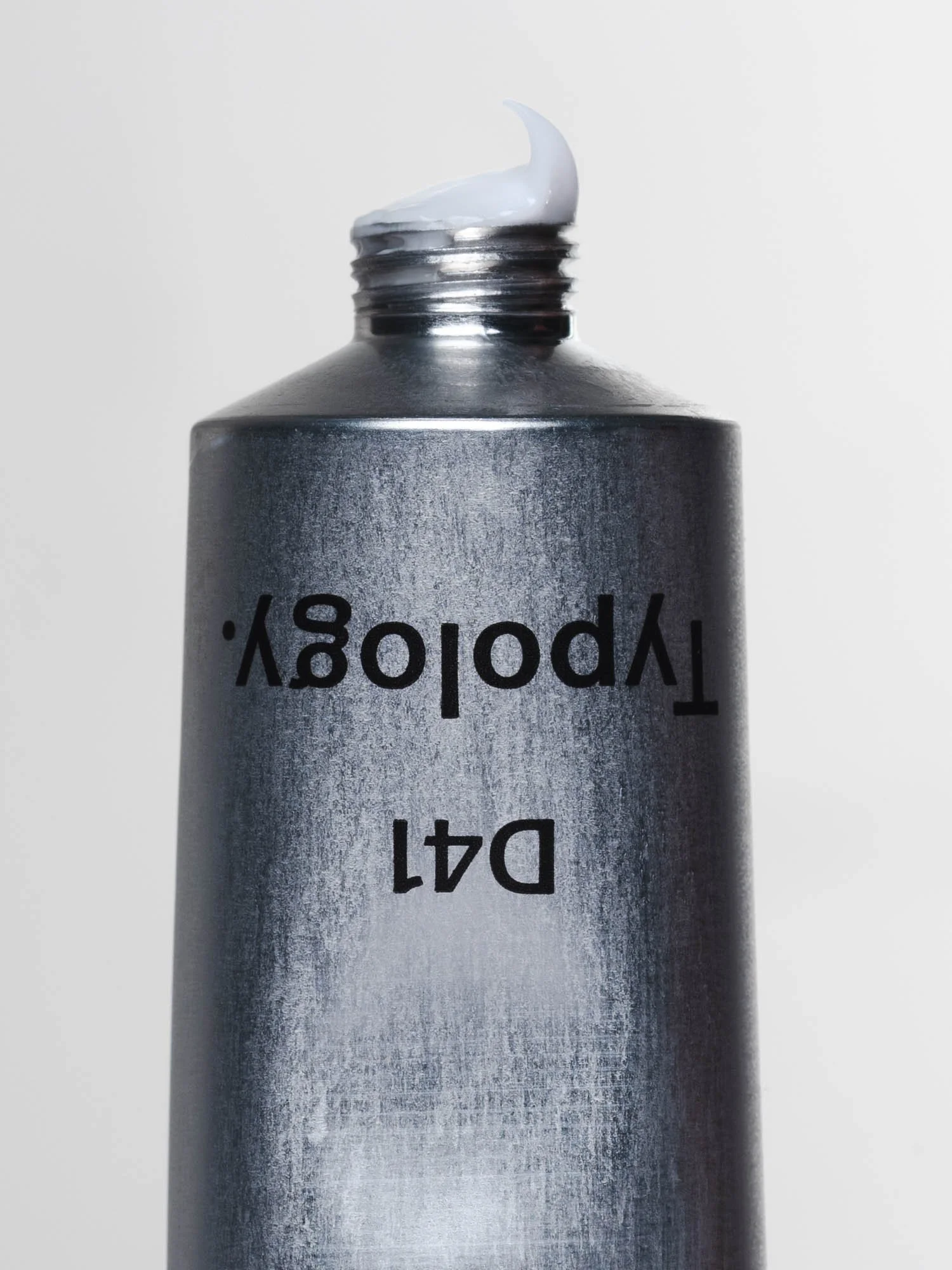 Un tube de crème de couleur métallique avec un contenu blanc visible à la sortie, et texte inversé sur l'emballage.