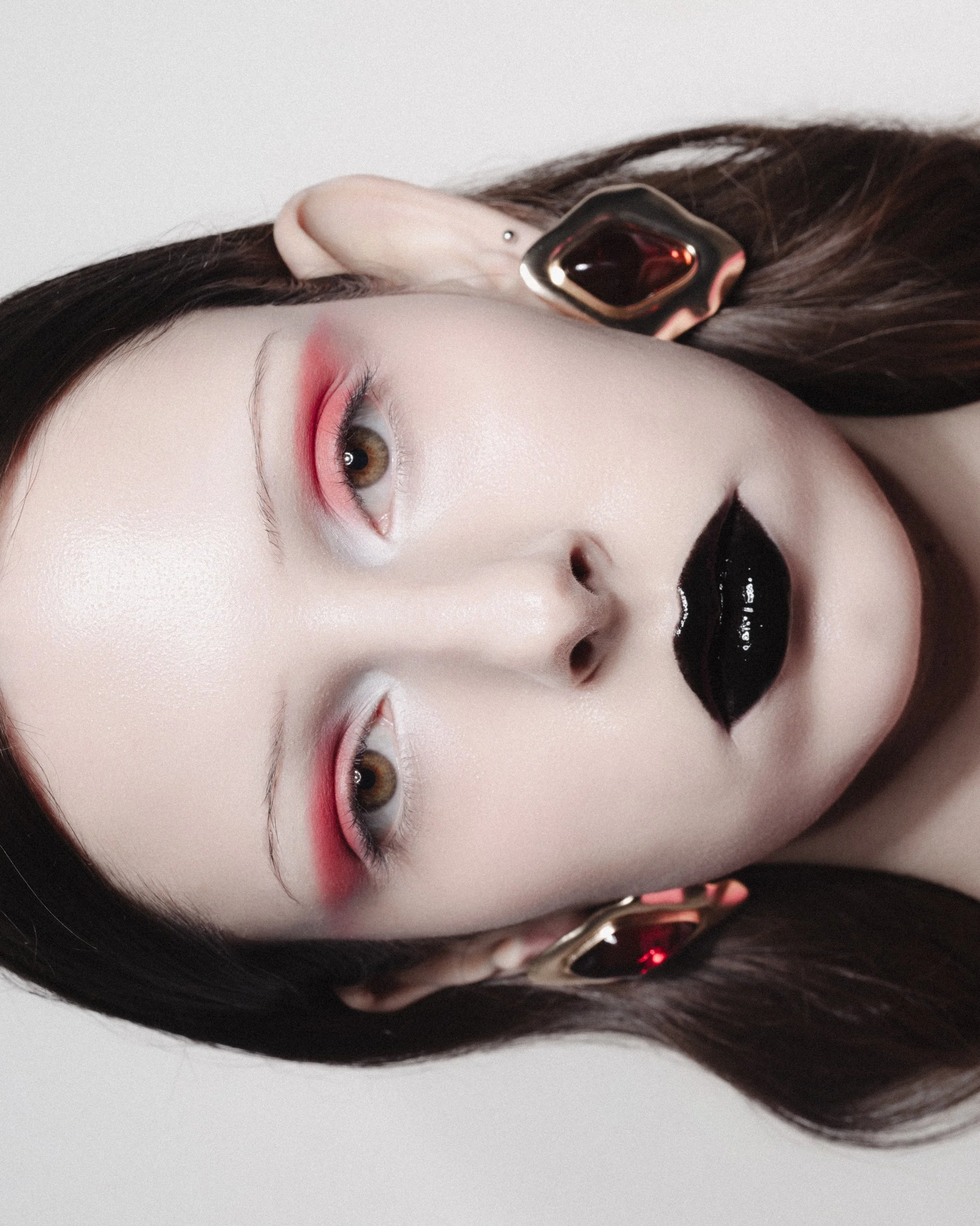 Portrait d'une femme avec maquillage artistique, lèvres noires et yeux avec maquillage rose, portant de grandes boucles d'oreilles dorées.