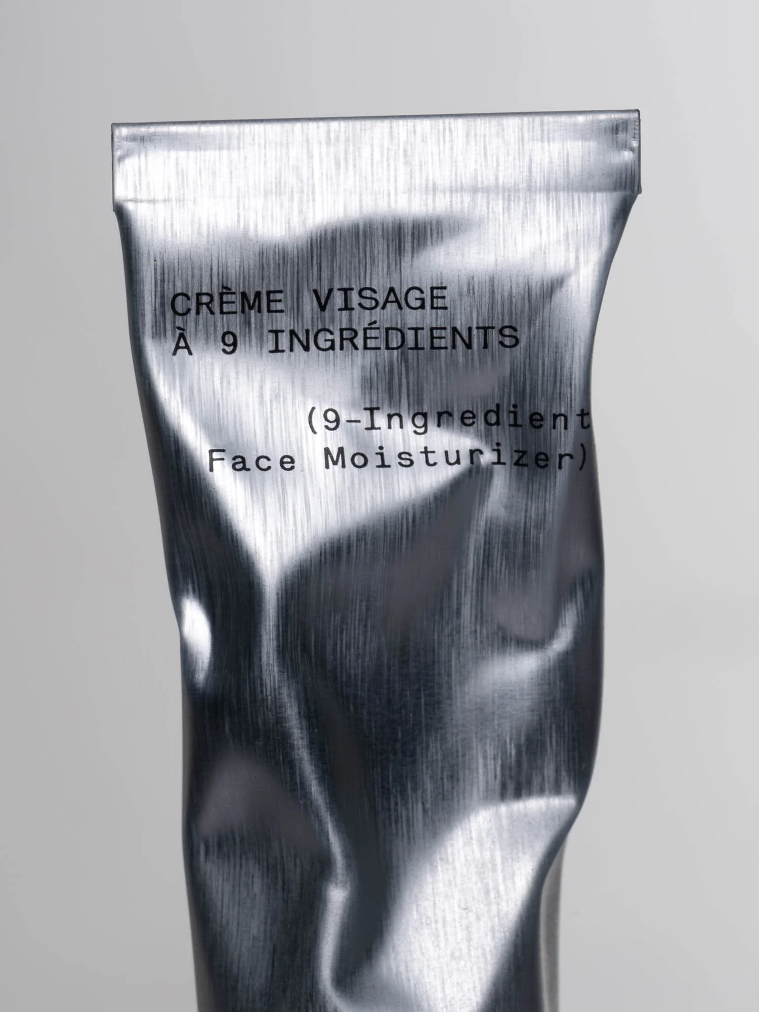 Tube de crème visage en emballage argenté, texte indiquant qu'elle contient une crème à 9 ingrédients.