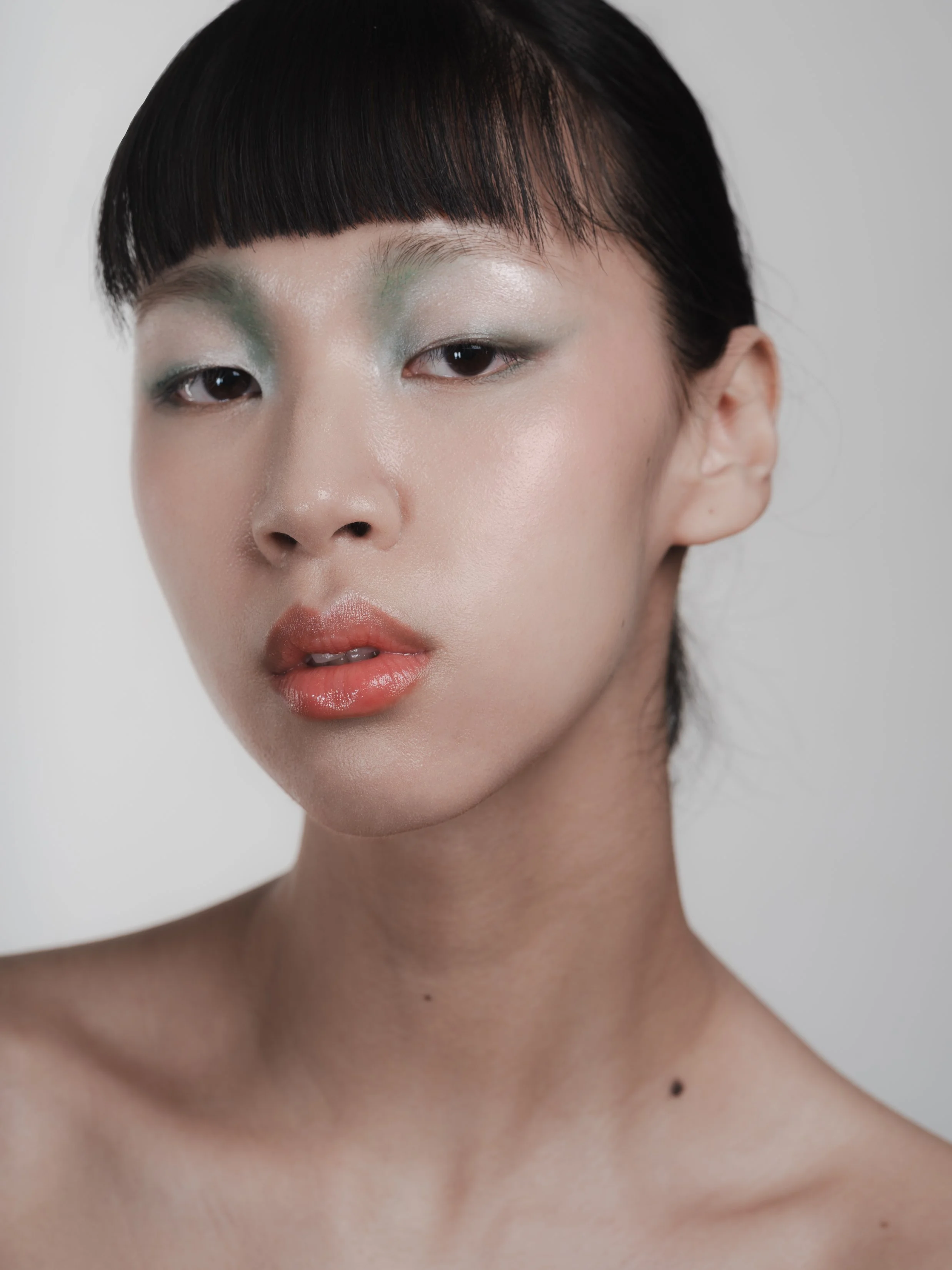 portrait d'une femme asiatique avec maquillage pastel et lèvres brillantes, cheveux noirs et coupe courte, fond blanc
