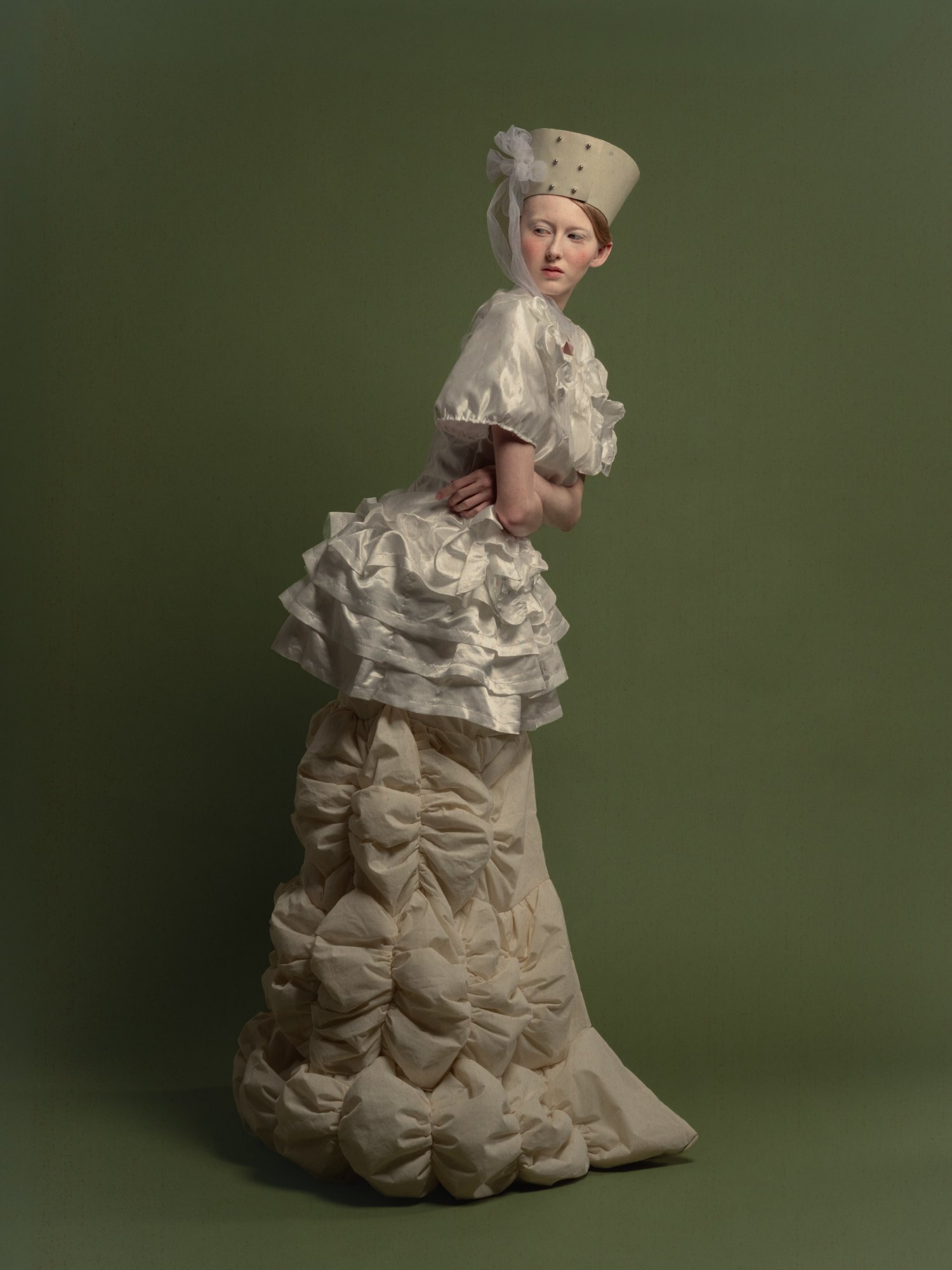 Jeune femme portant une robe de style antique en satin avec des volants et un chapeau orné de perles et d'une pièce en tissu blanc.