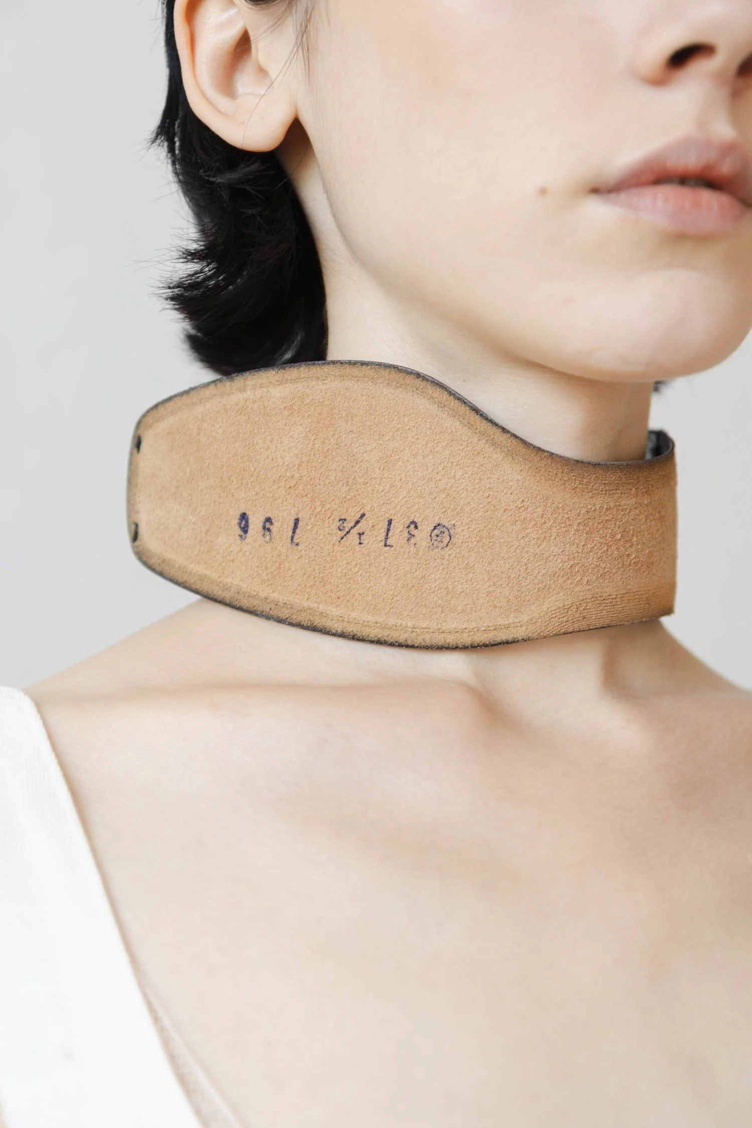 Une femme portant un collier large en cuir beige avec des numéros et des symboles imprimés dessus.