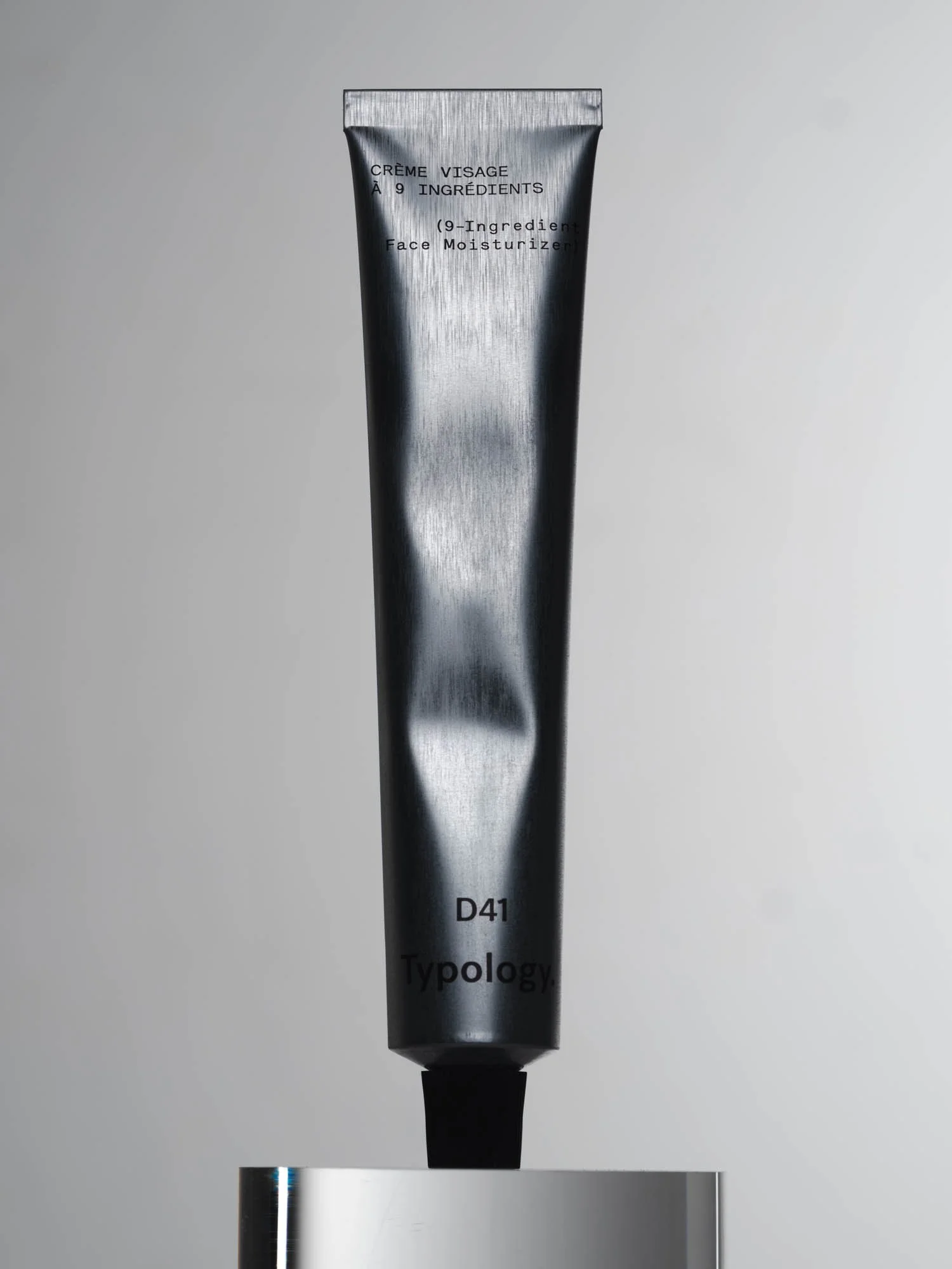 Tube de crème visage aligné en vertical sur fond gris clair.